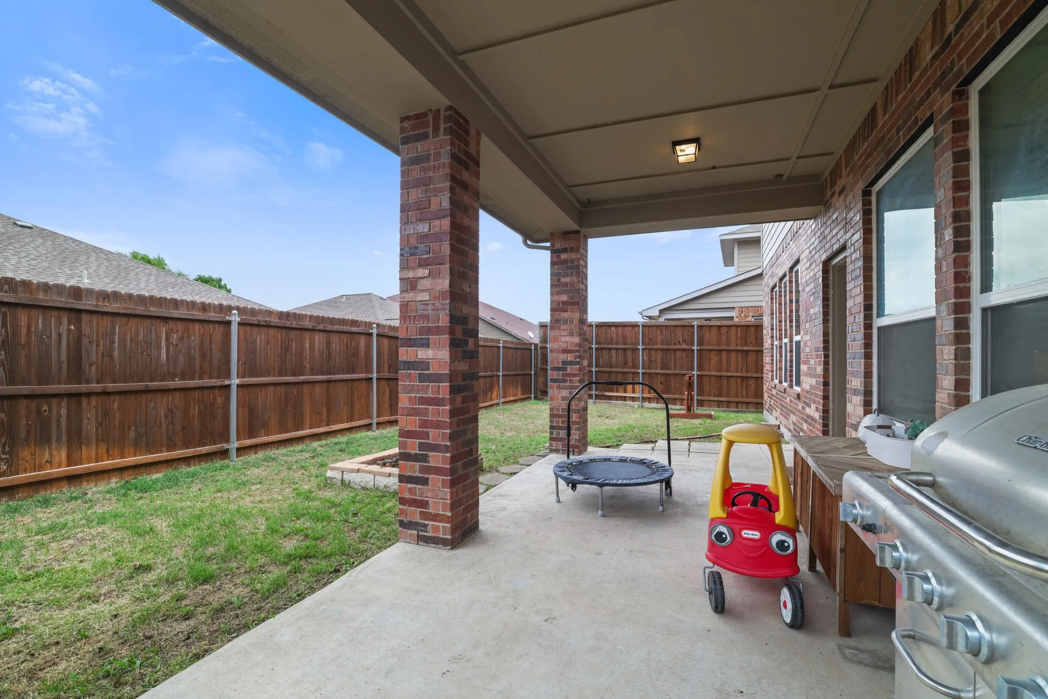 Covered concrete patio with brick support columns, a wood privacy fence, and a built-in fire pit