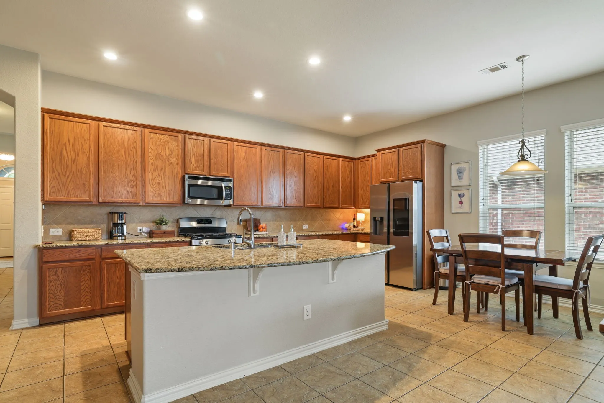 Kitchen featuring wood cabinetry, stainless steel appliances, a center island with a granite-style countertop, and tile flooring