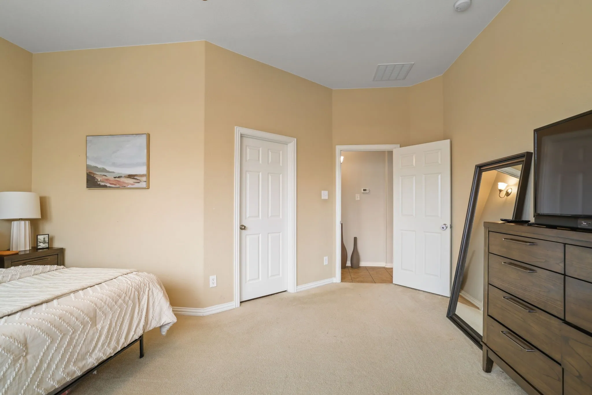 Light beige carpeting, warm neutral wall paint, two white paneled doors, and a ceiling-mounted light fixture