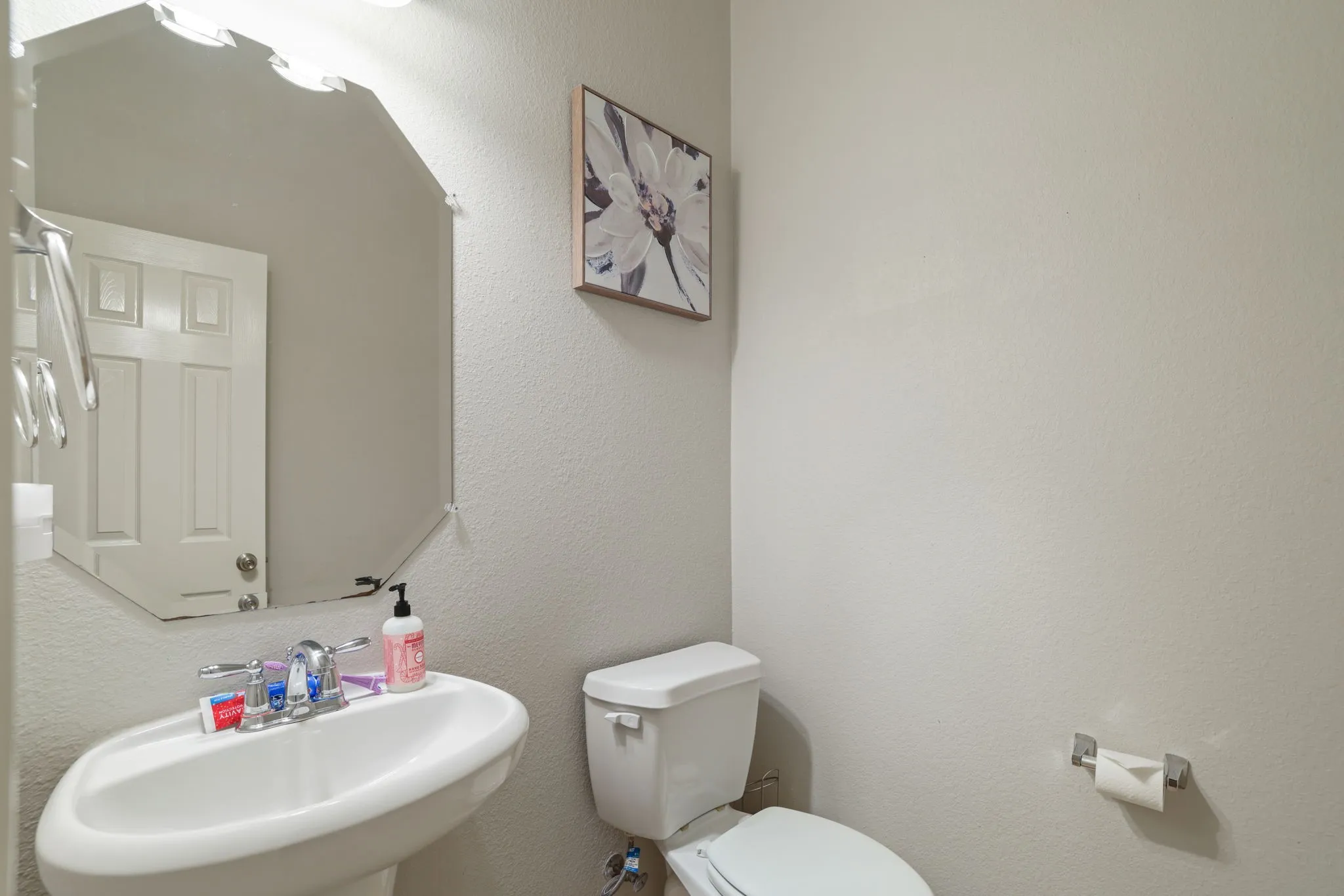 Pedestal sink with chrome faucet, octagonal wall mirror, and a white toilet