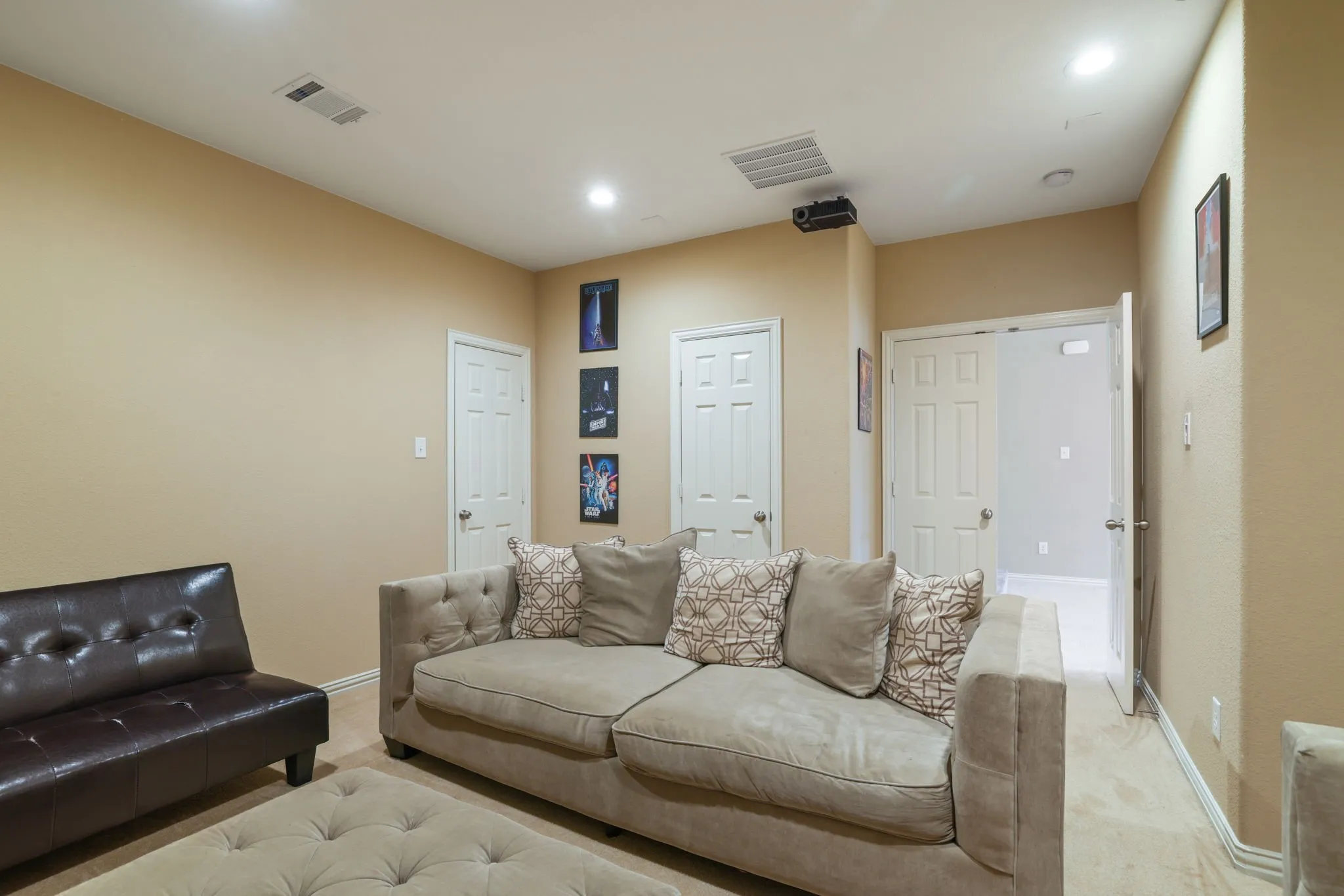 Recessed ceiling lighting, ceiling-mounted projector, wall-mounted air vent, neutral wall paint, and white paneled doors