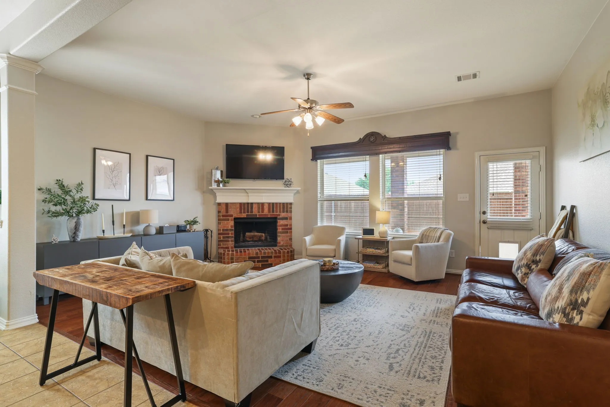 Hardwood flooring, brick fireplace with mantel, ceiling fan, crown molding, and a built-in media console