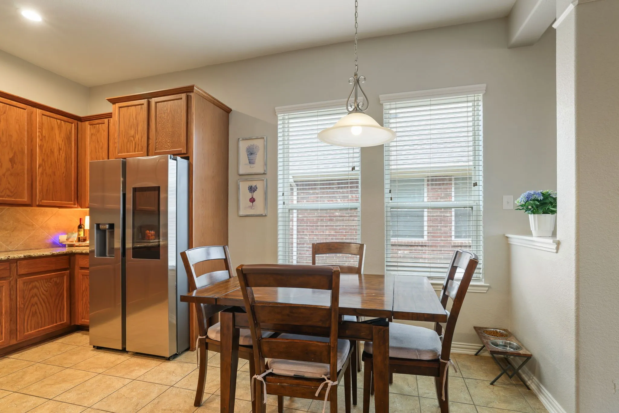 Kitchen featuring wood cabinetry, stainless steel refrigerator, tile flooring, and a dining area with pendant lighting
