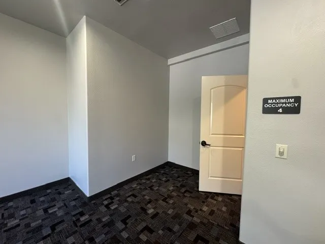Wall-to-wall patterned carpet flooring, neutral painted walls, and a white interior door with a black handle