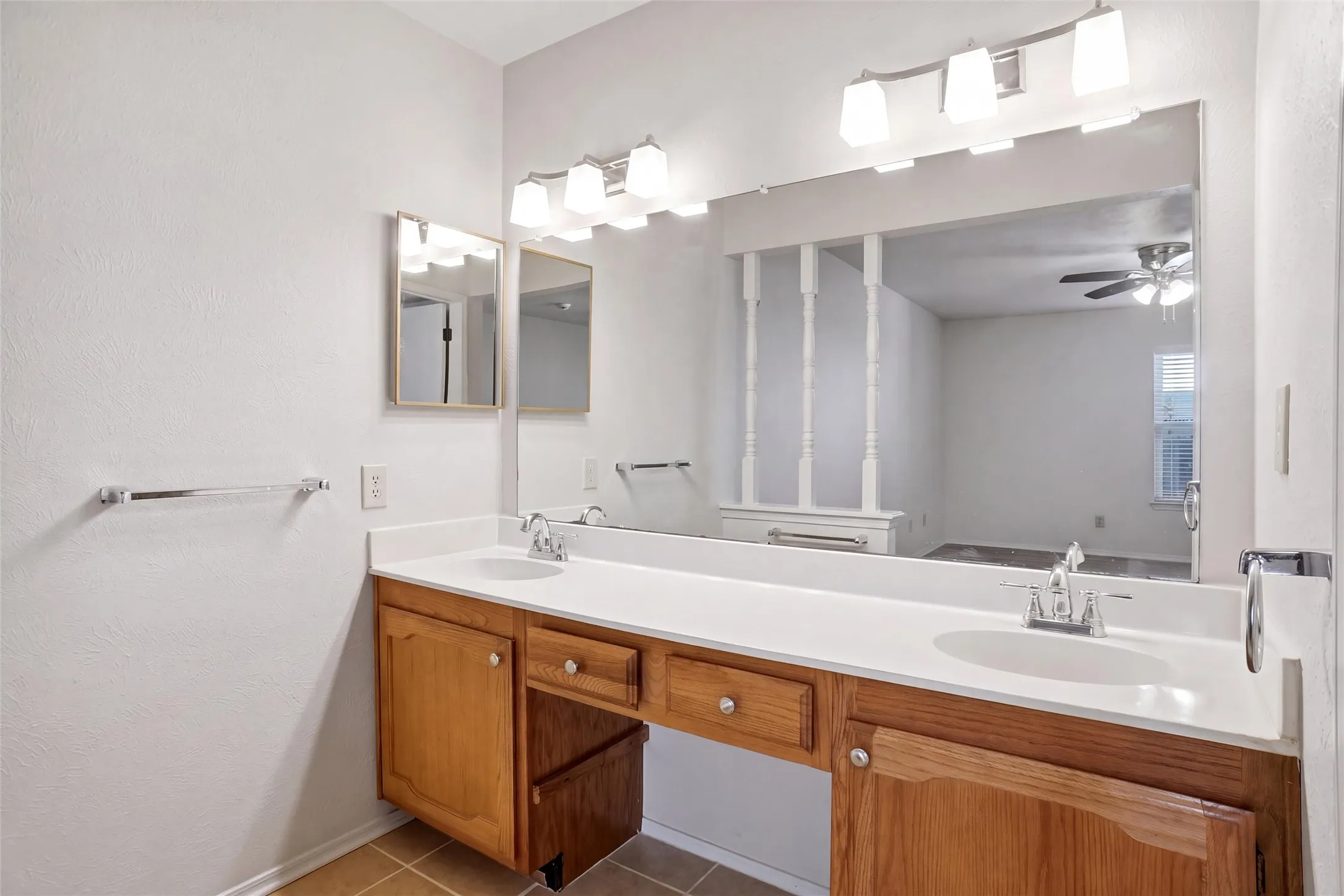 Dual basin vanity with wood-finish cabinetry, white countertop, and prominent wall-mounted mirror