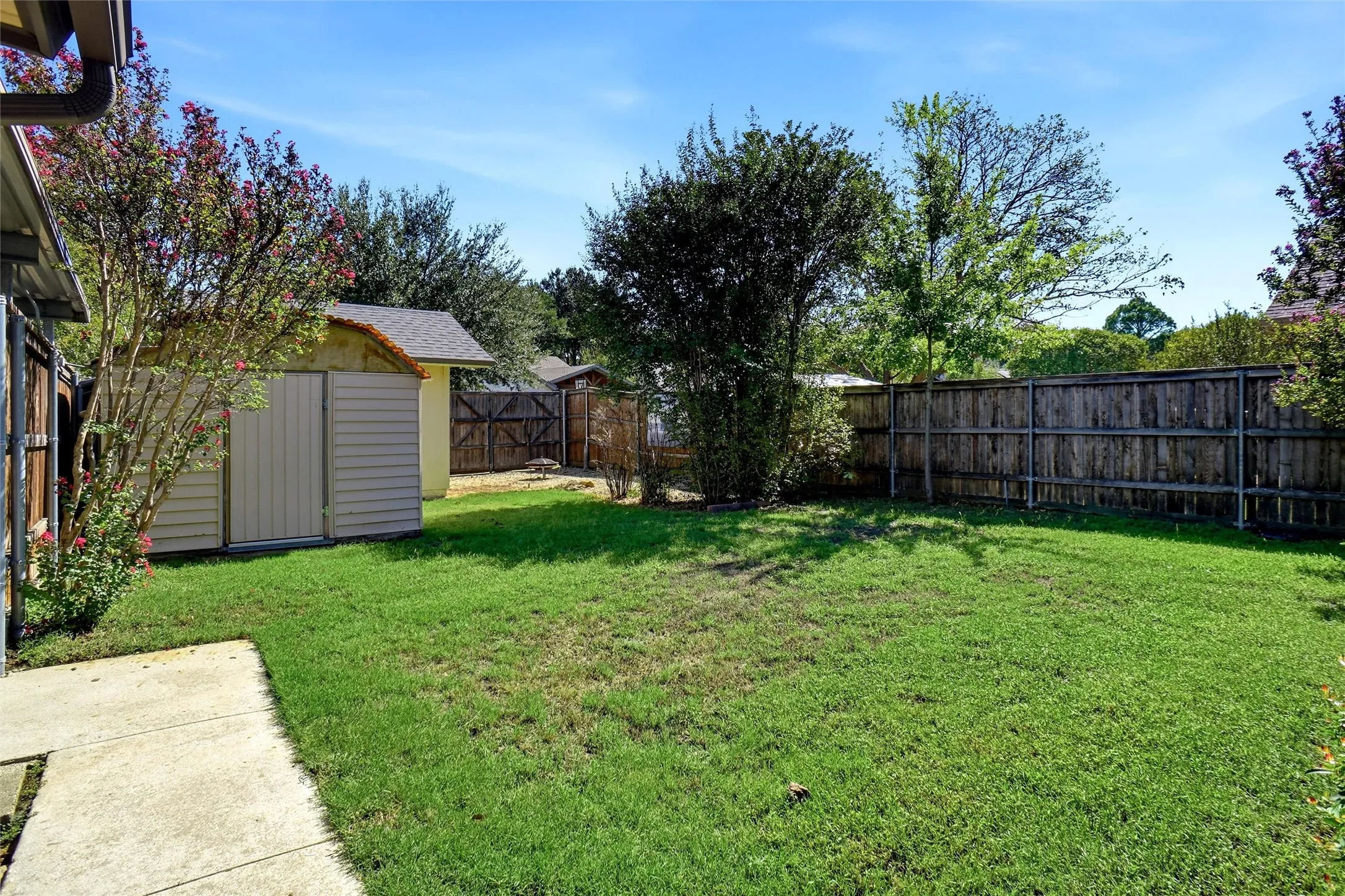 Expansive backyard featuring a manicured lawn, established privacy fencing, mature trees, and a detached storage shed