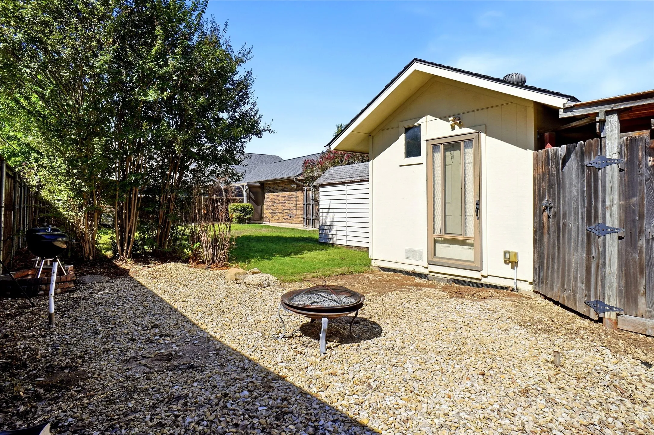 Gravel patio area with a fire pit, privacy fencing, and mature landscaping