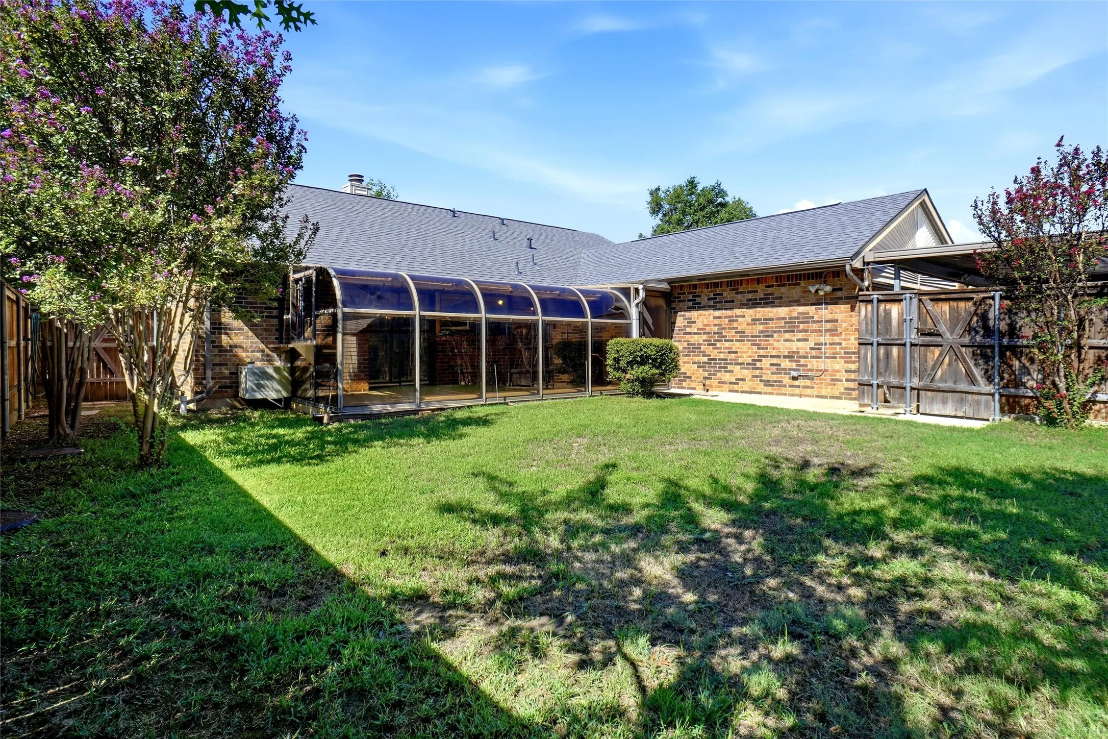 Enclosed pool structure, brick exterior, shingle roofing, and mature shrubbery