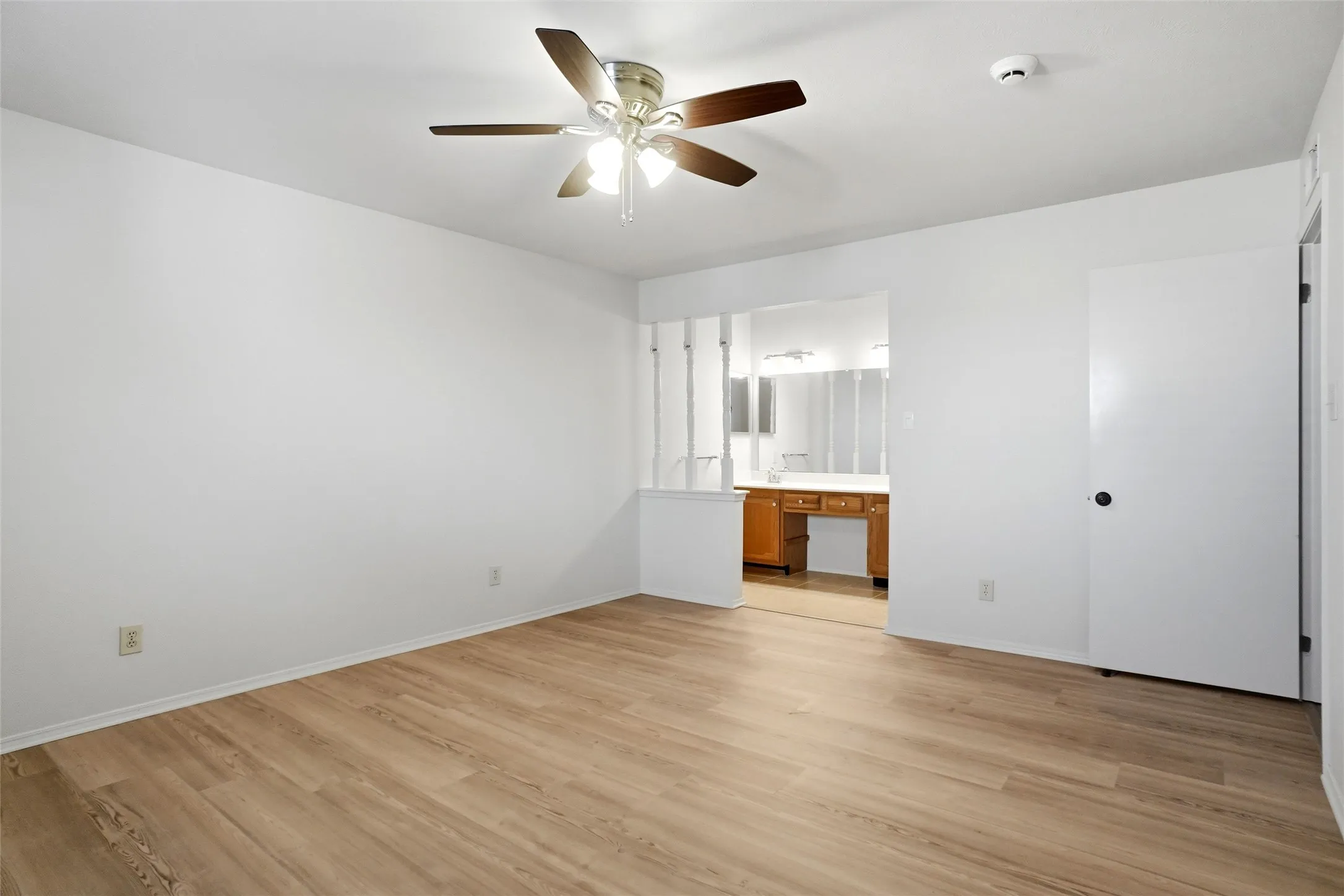 Wood-finish flooring, ceiling fan, white interior walls, white door, and built-in vanity with wood-finish cabinetry