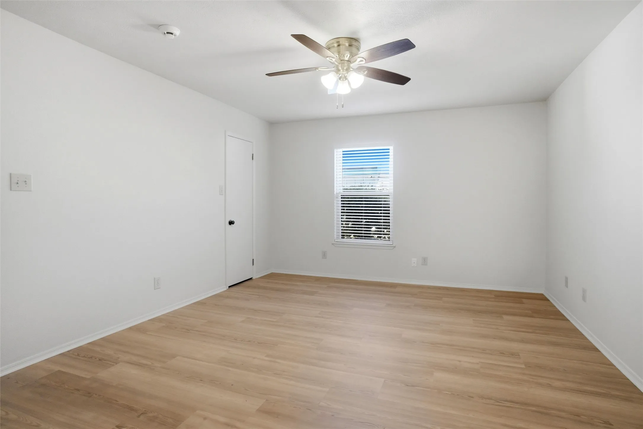 Bright interior with wood-finish flooring, a ceiling fan with integrated lighting, and a single window with blinds