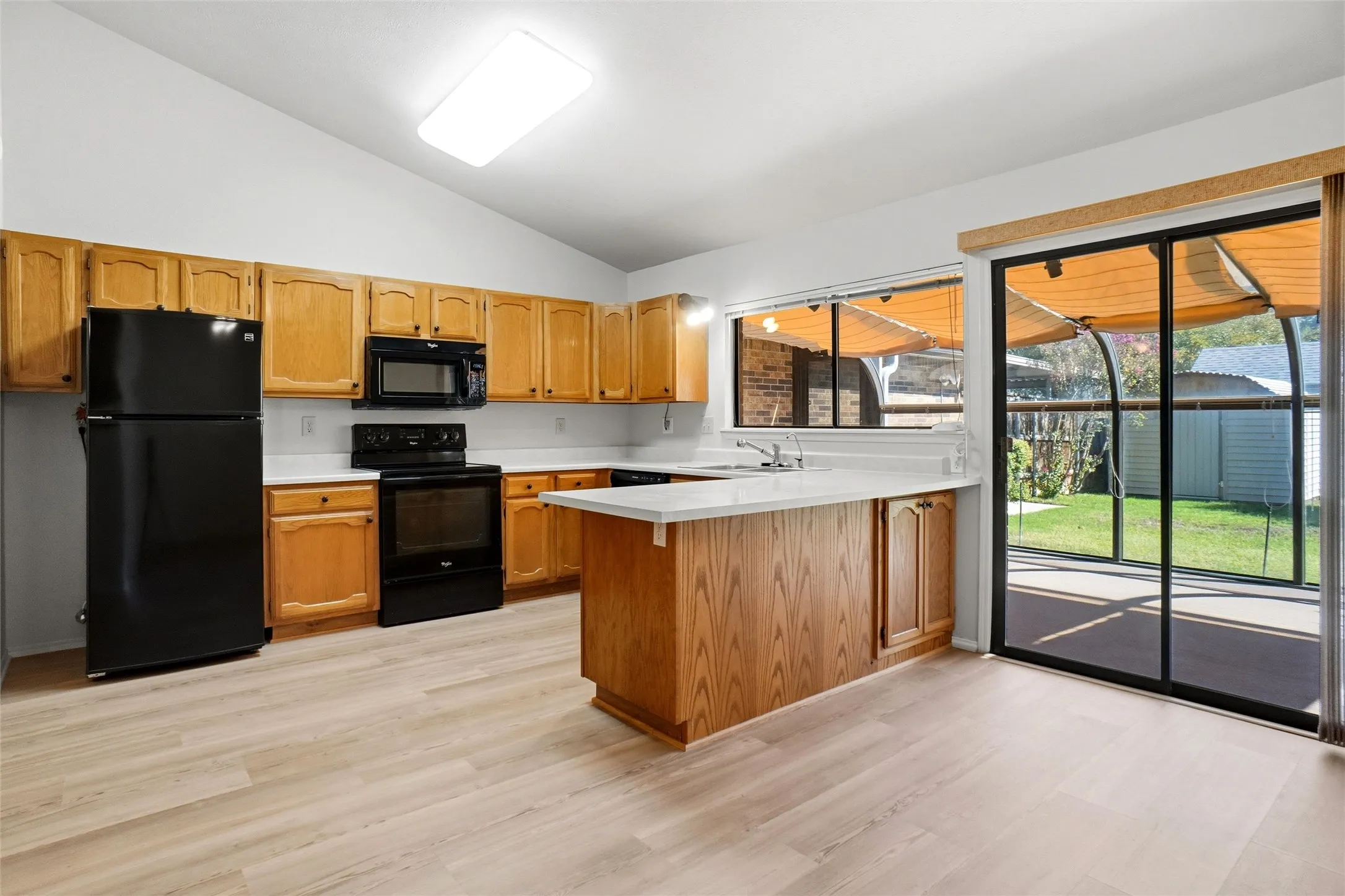 Kitchen featuring wood-finish flooring, light wood cabinetry, white countertops, and a black appliance suite