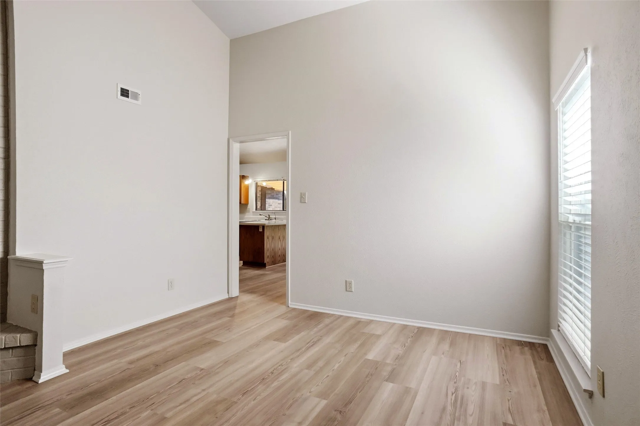 Vaulted ceiling, wood-finish flooring, white walls, window with blinds, and white trim