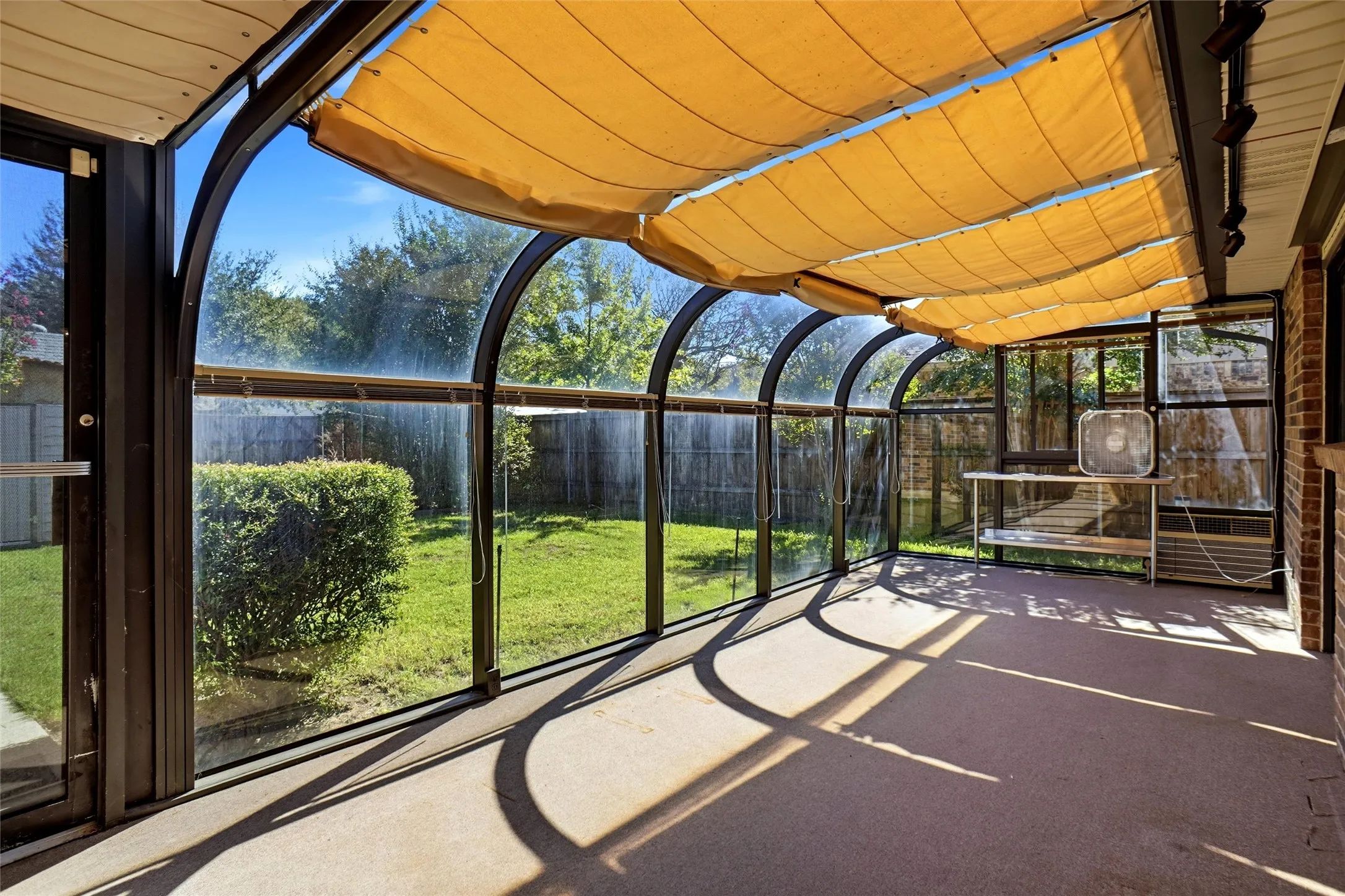 Arched glass enclosure with retractable fabric shades, brick exterior wall, and concrete flooring