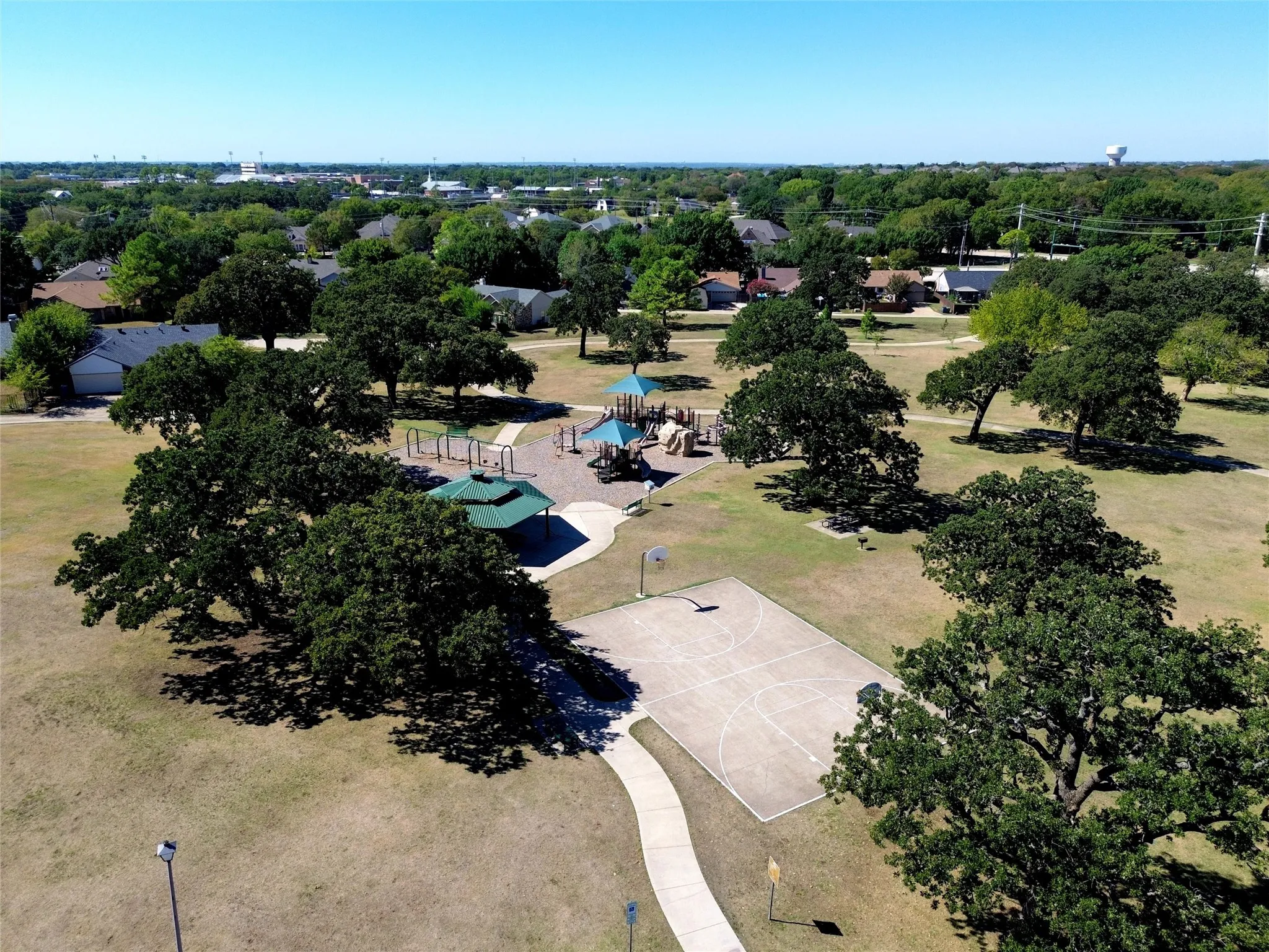 Expansive park featuring a basketball court, playground equipment, covered pavilion, and mature trees