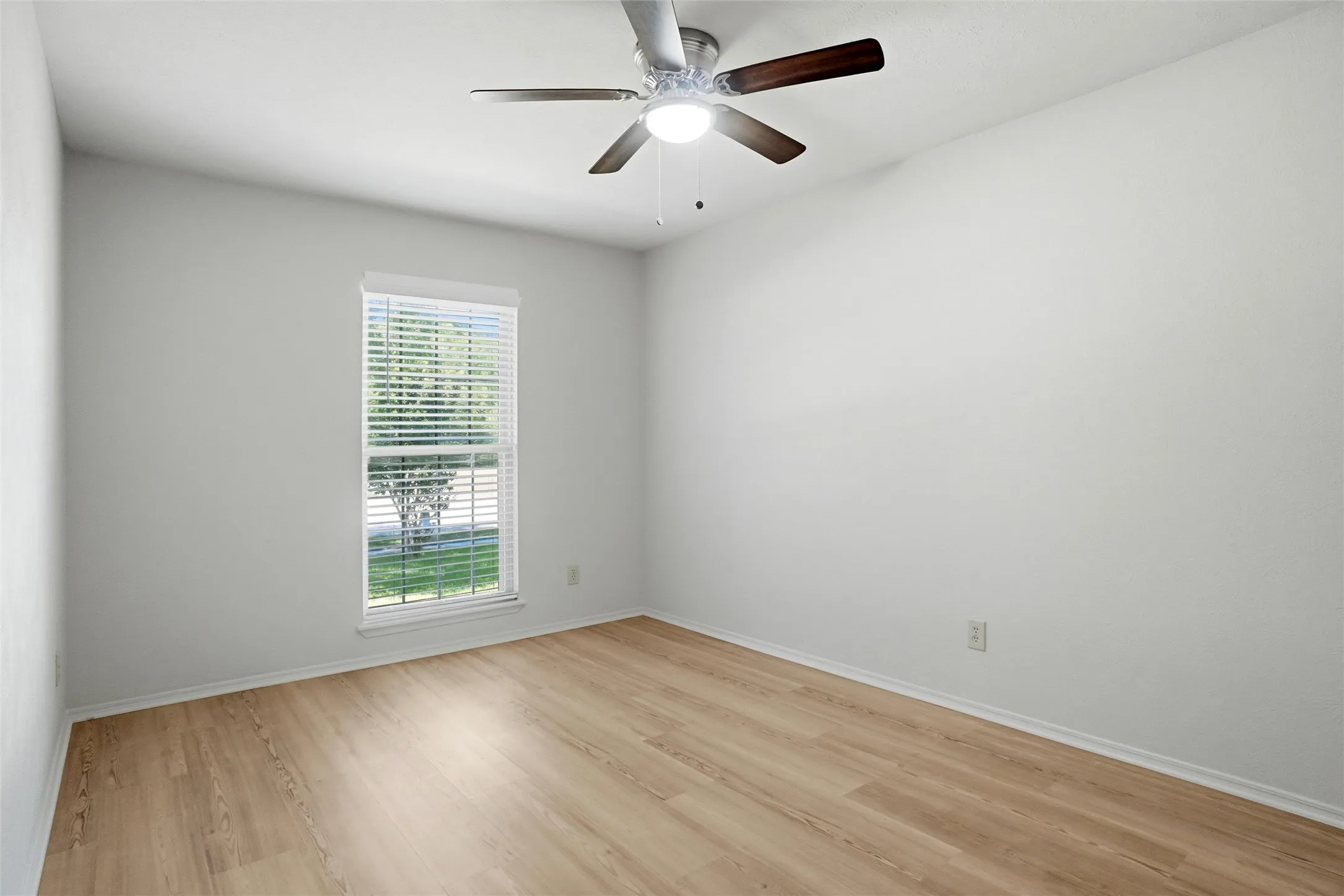 Recessed window with blinds, wood-finish flooring, and a ceiling fan with light fixture