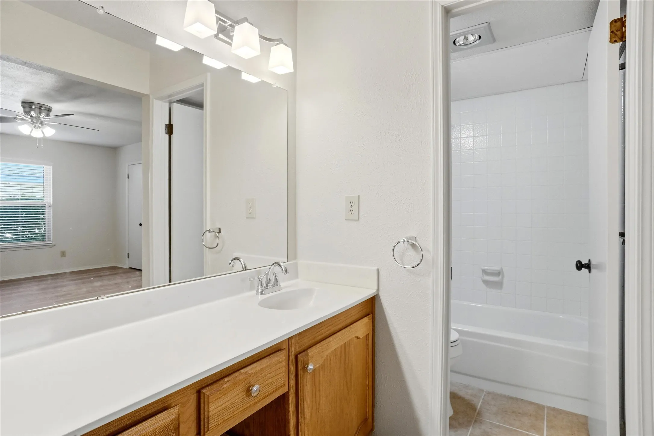 Bathroom vanity with a single sink, light wood-finish cabinetry, and a full-width mirror