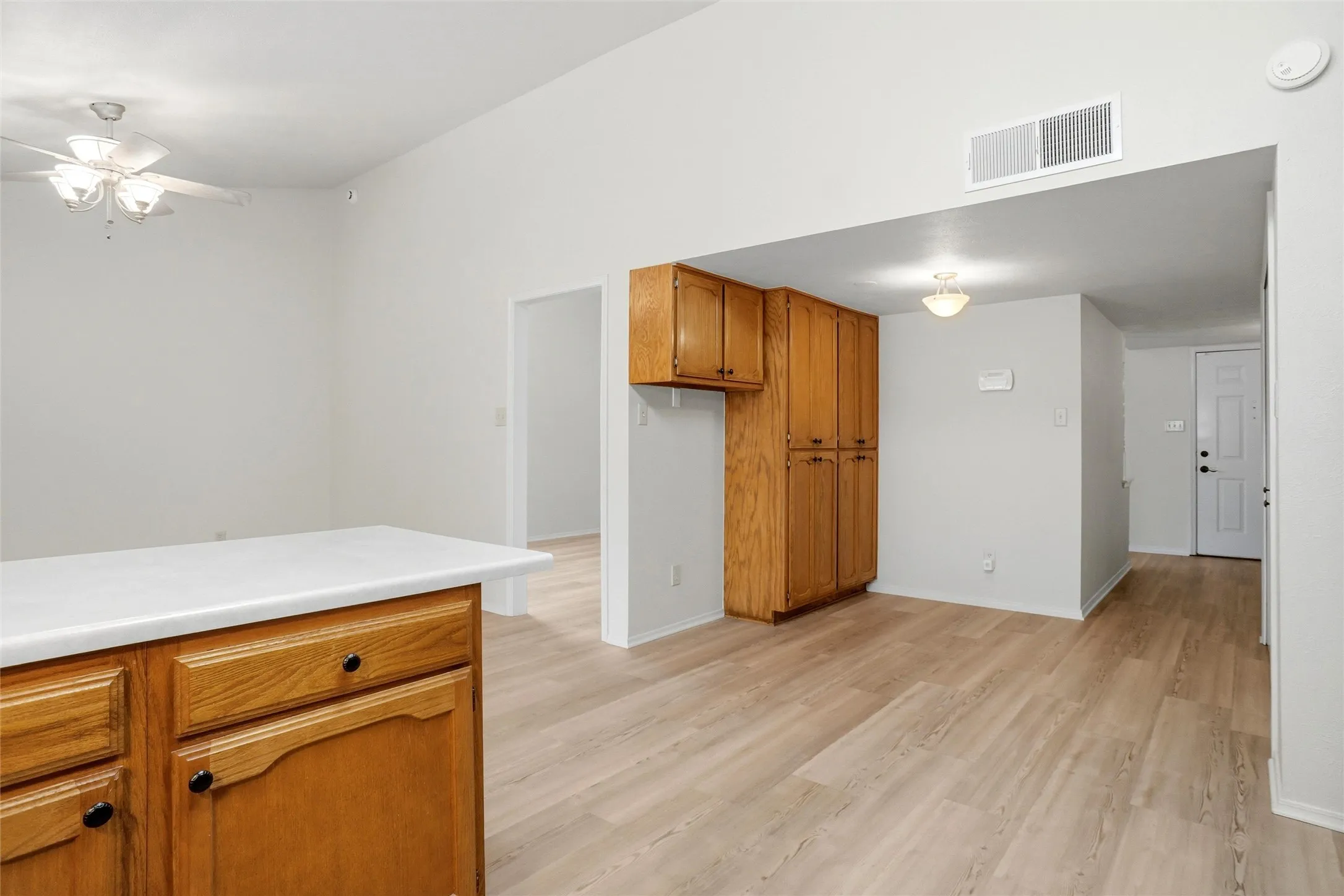 Vaulted ceiling, ceiling fan with light fixture, wood-finish flooring, wood cabinetry with black hardware, and white countertop