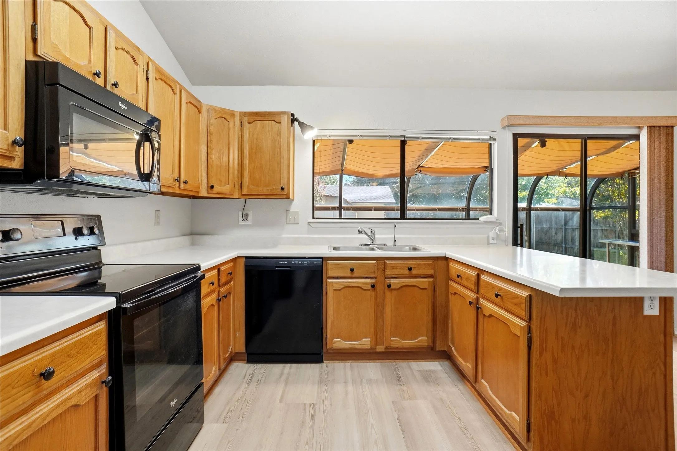 Kitchen featuring wood cabinetry, white countertops, black appliances, and wood-finish flooring