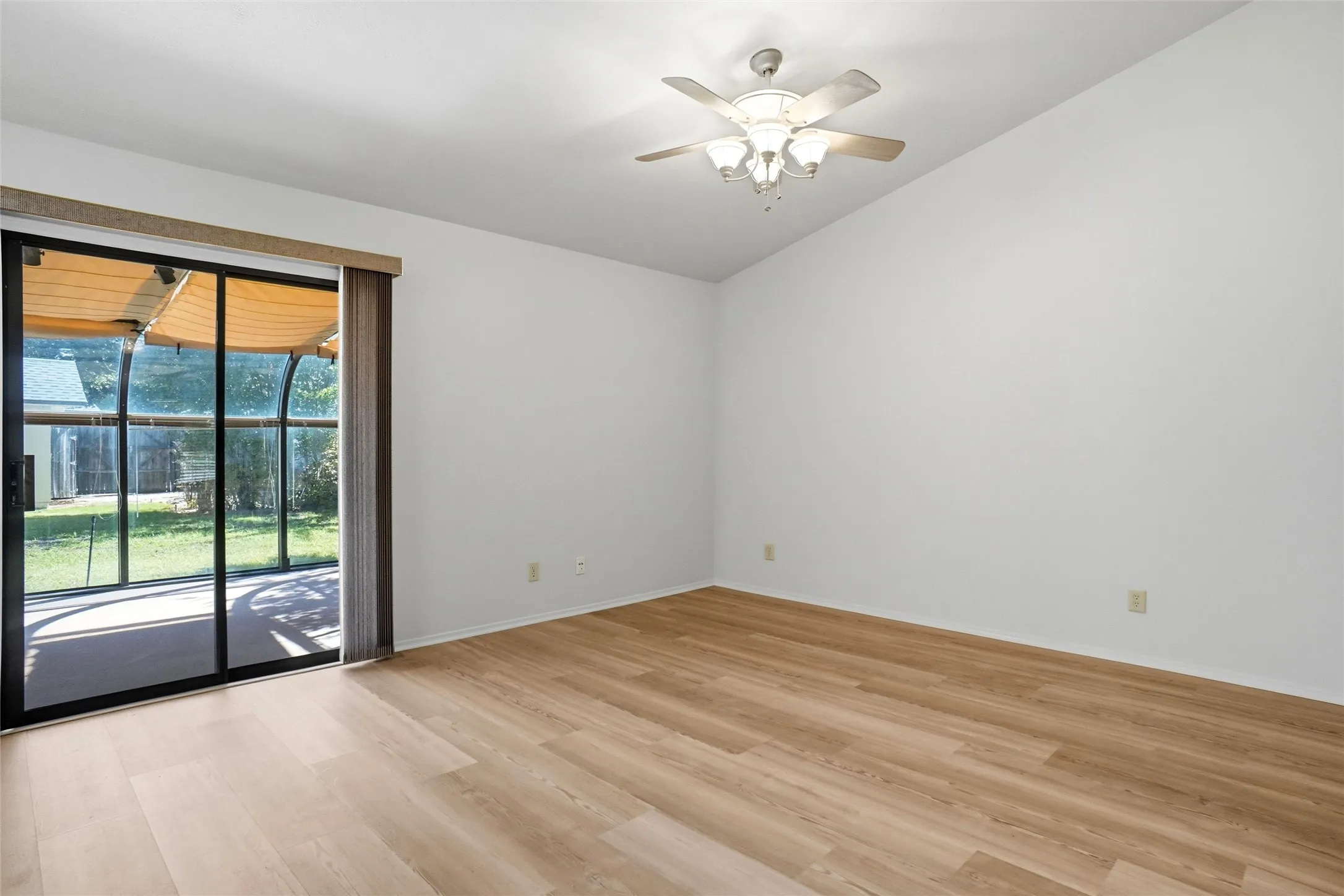 Vaulted ceiling, wood-finish flooring, ceiling fan with integrated lighting, and sliding glass door to a screened patio