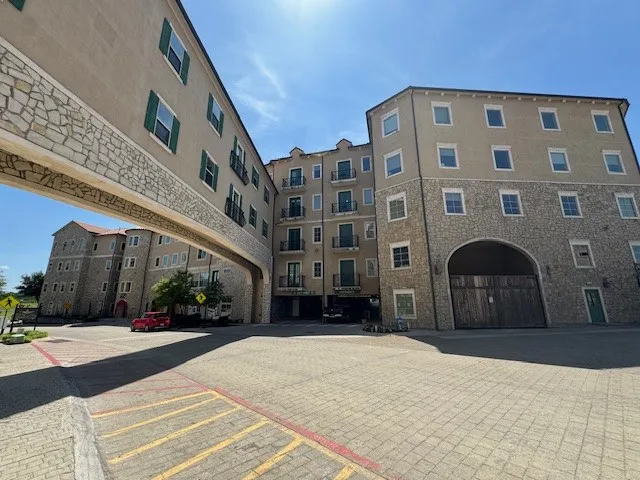 Multi-story building featuring a stone and stucco exterior, arched entryway, green shutters, and balcony railings