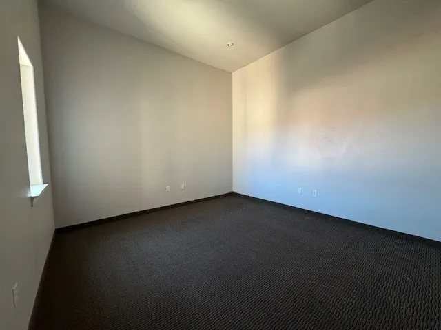 Recessed ceiling lighting, textured wall finish, and a window with a white sill, complemented by dark patterned carpeting