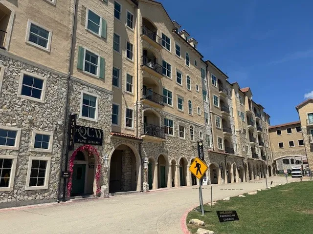 Multi-story building featuring stone and stucco exterior, arched walkways, decorative iron balconies, and prominent window shutters