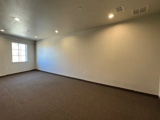 Spacious room featuring neutral wall tones, recessed lighting, a multi-pane window, and patterned carpet flooring