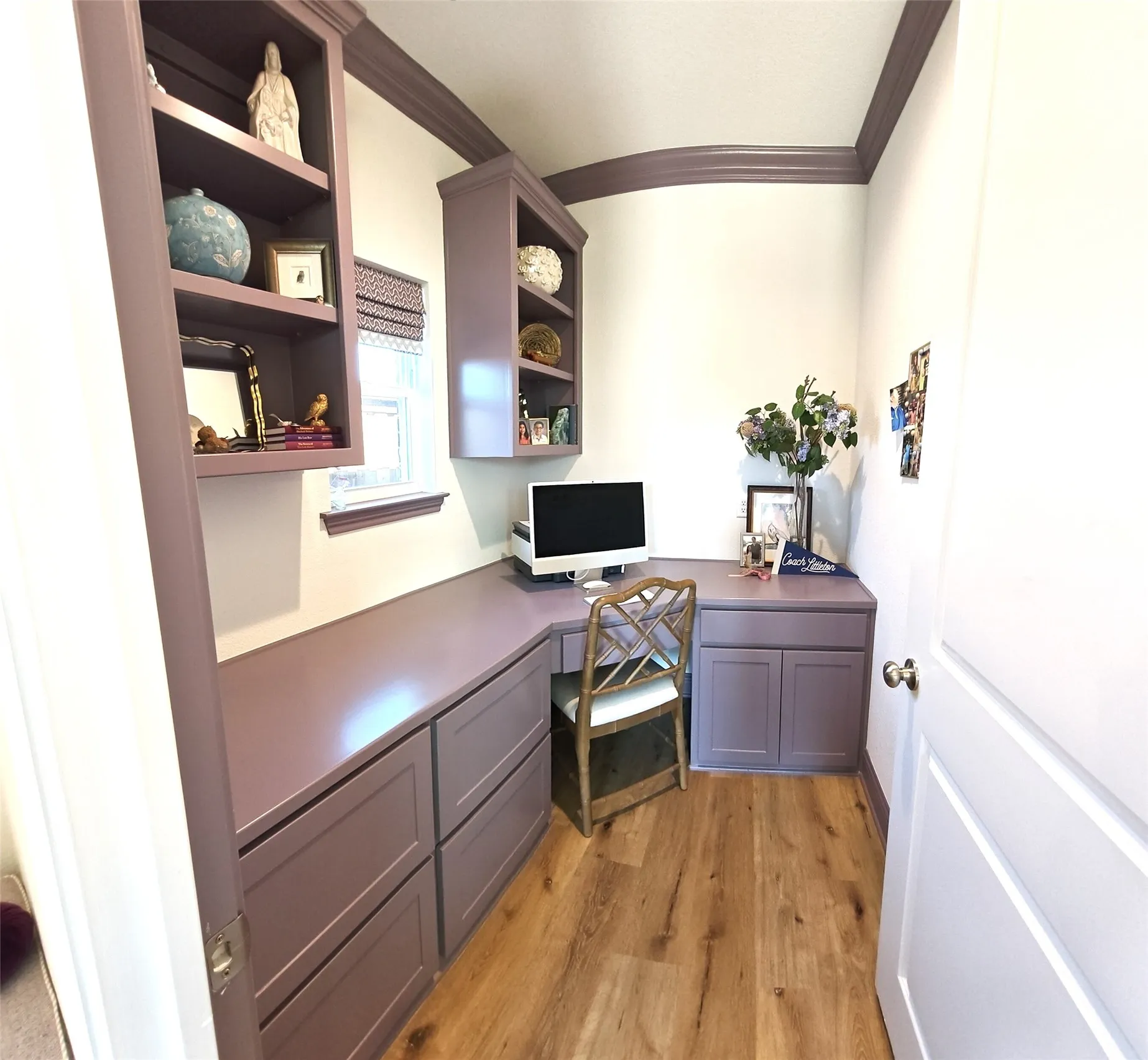 Built-in desk with extensive cabinetry, wall-mounted shelving, wood-finish flooring, and crown molding