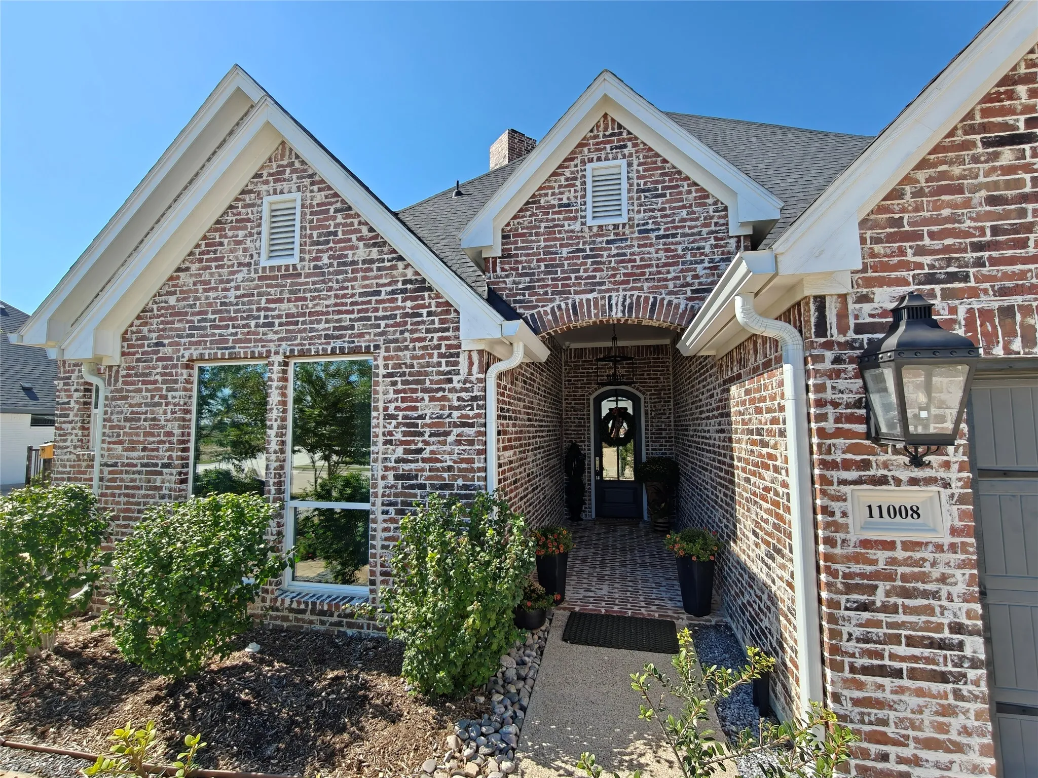 Brick exterior with white mortar, arched entry, integrated exterior lighting, and a paved walkway