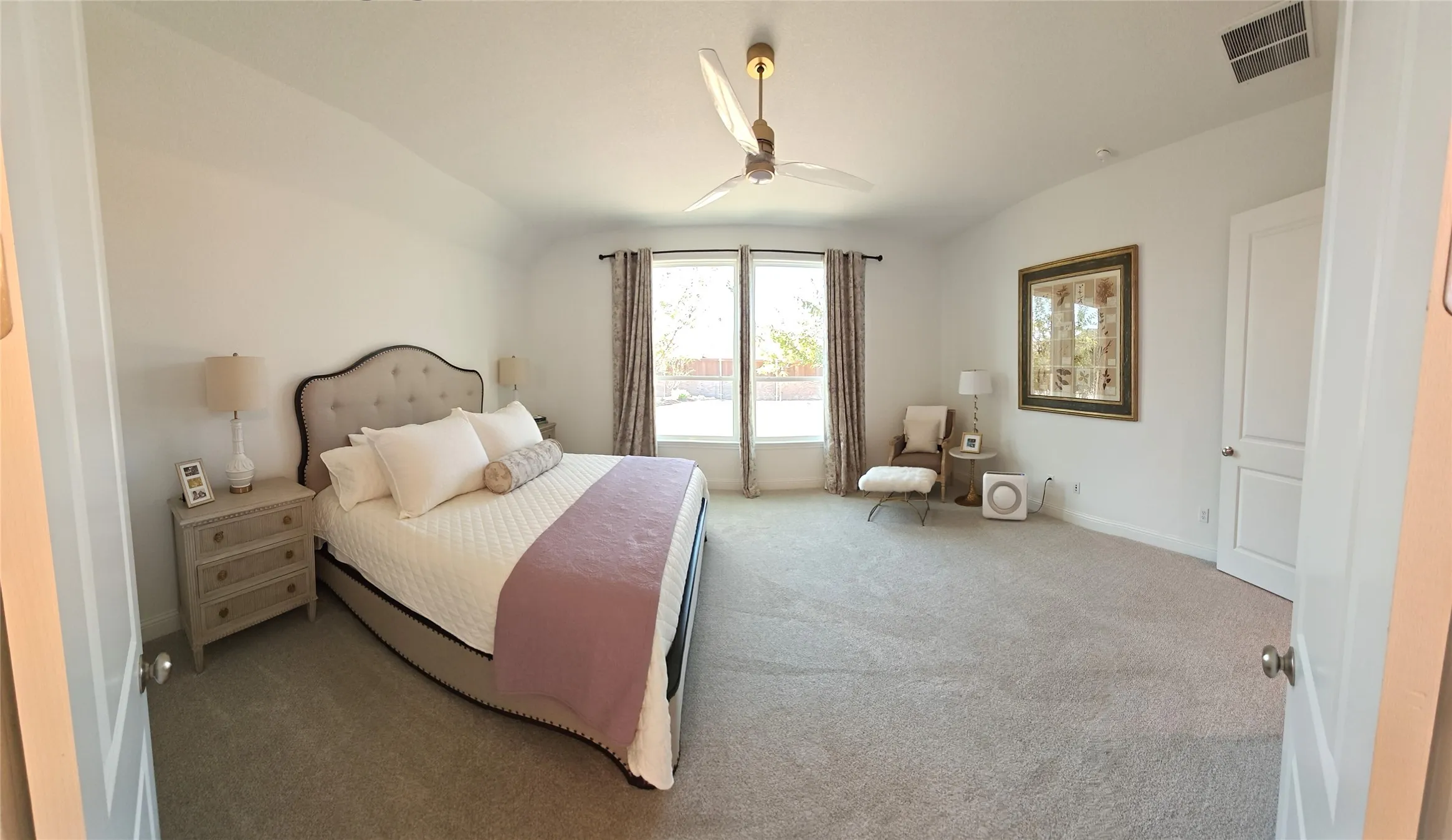 Vaulted ceiling with a ceiling fan, light gray carpeting, and large windows with privacy drapes