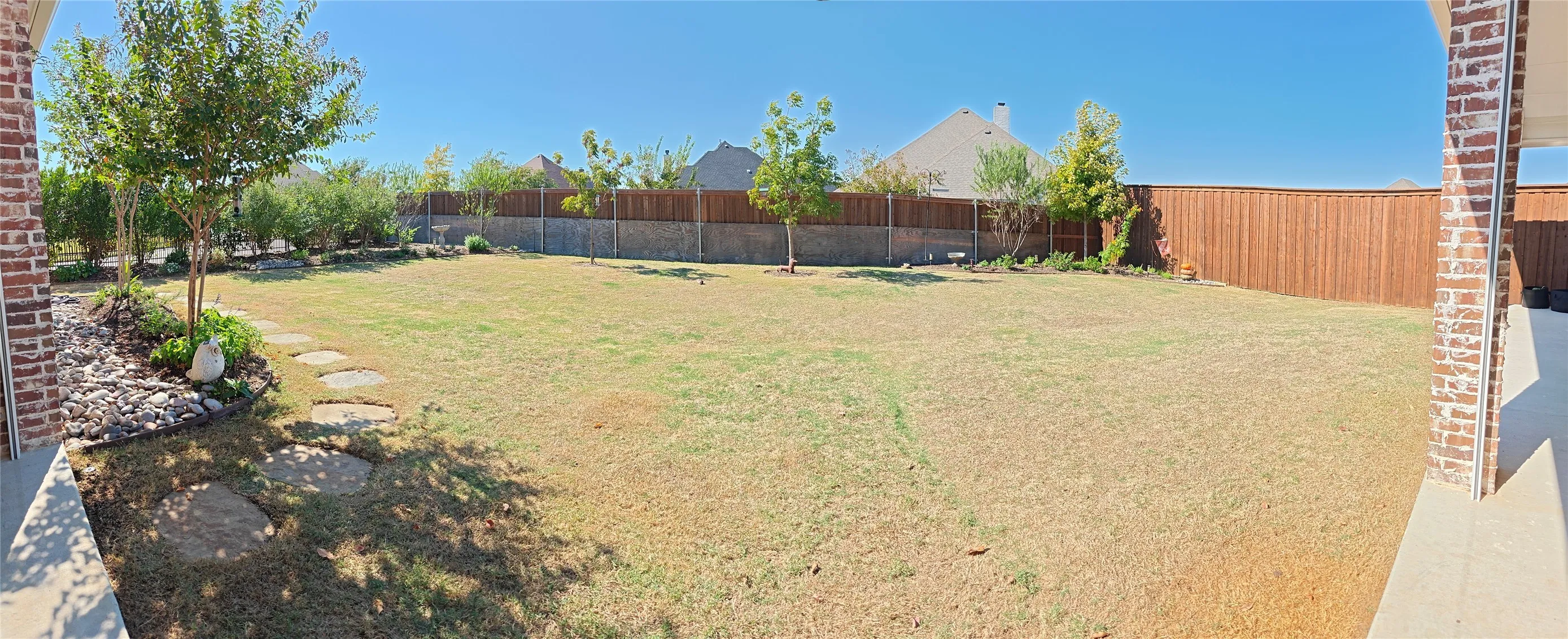 Expansive backyard featuring a fenced perimeter, stone pathway, and varied plantings