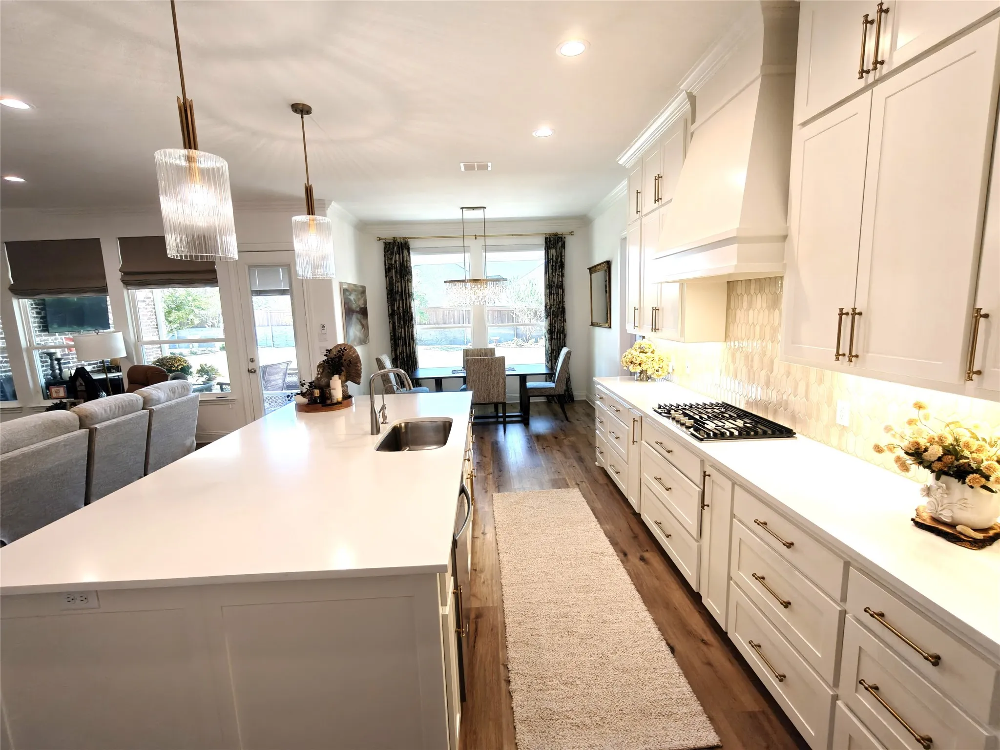 Kitchen island with integrated sink, white cabinetry with gold-tone hardware, gas cooktop, and wood-finish flooring