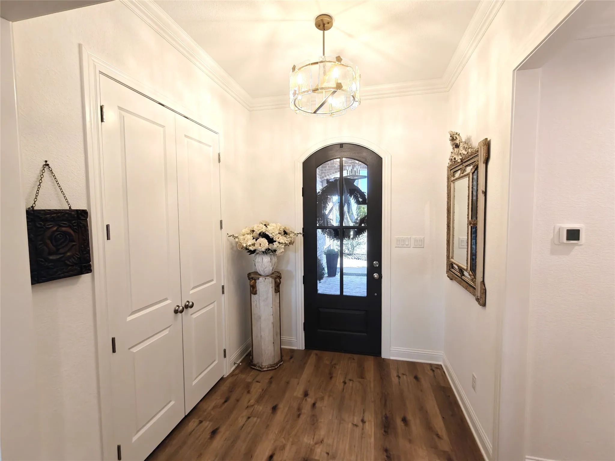 Arched glass panel entry door, wood-finish flooring, recessed lighting, double-door closet, and crown molding