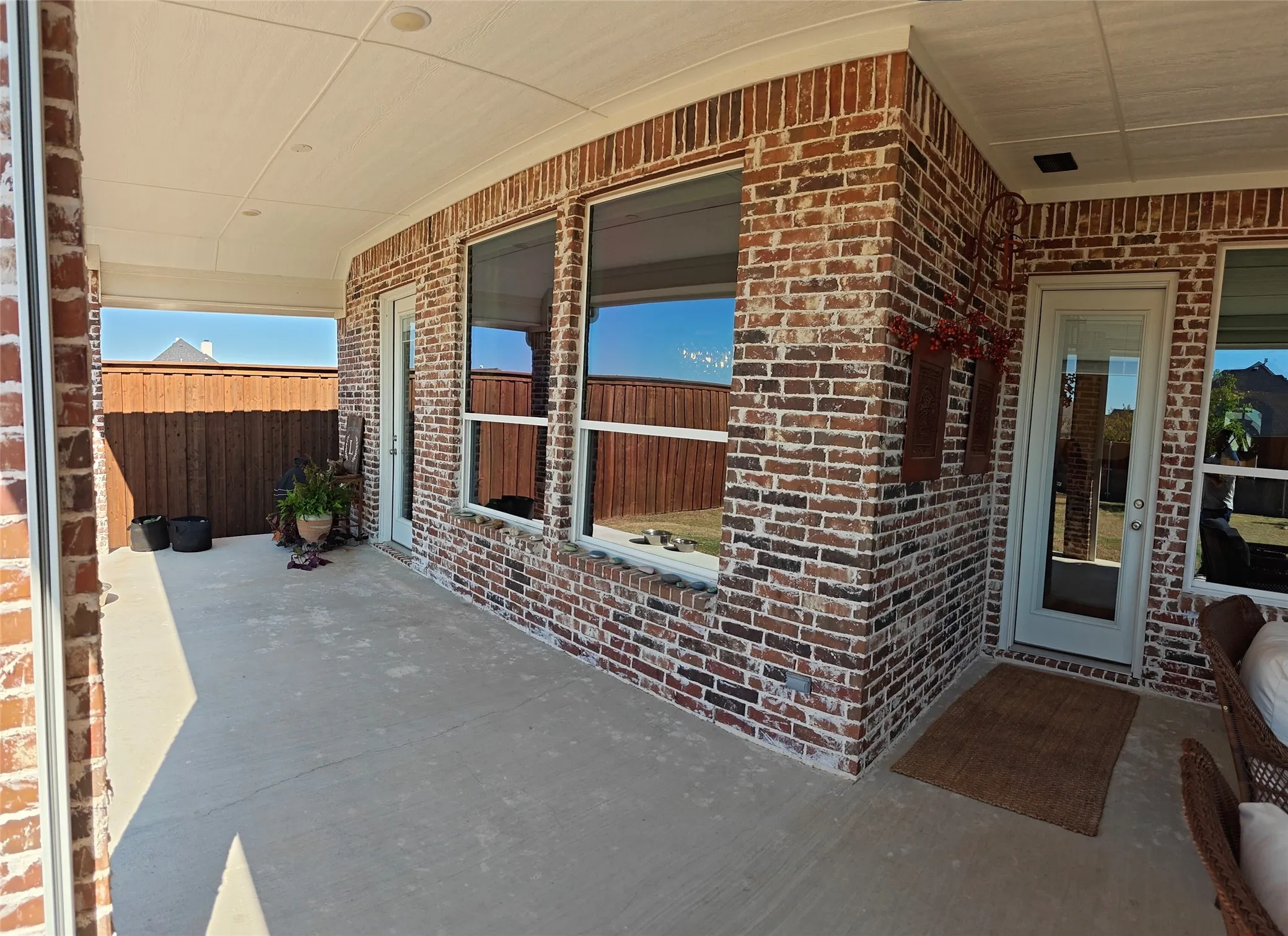 Covered patio featuring a concrete surface, brick exterior, multiple windows, and a glass-paneled door