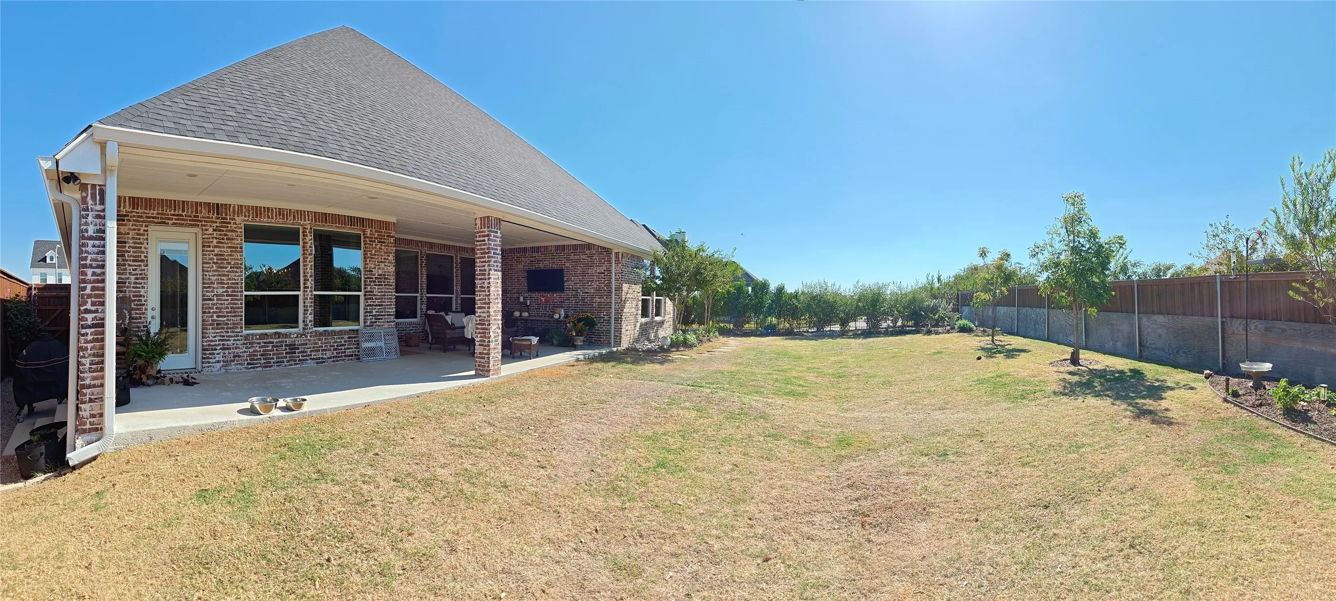Expansive backyard with a covered patio, brick exterior, and a privacy fence