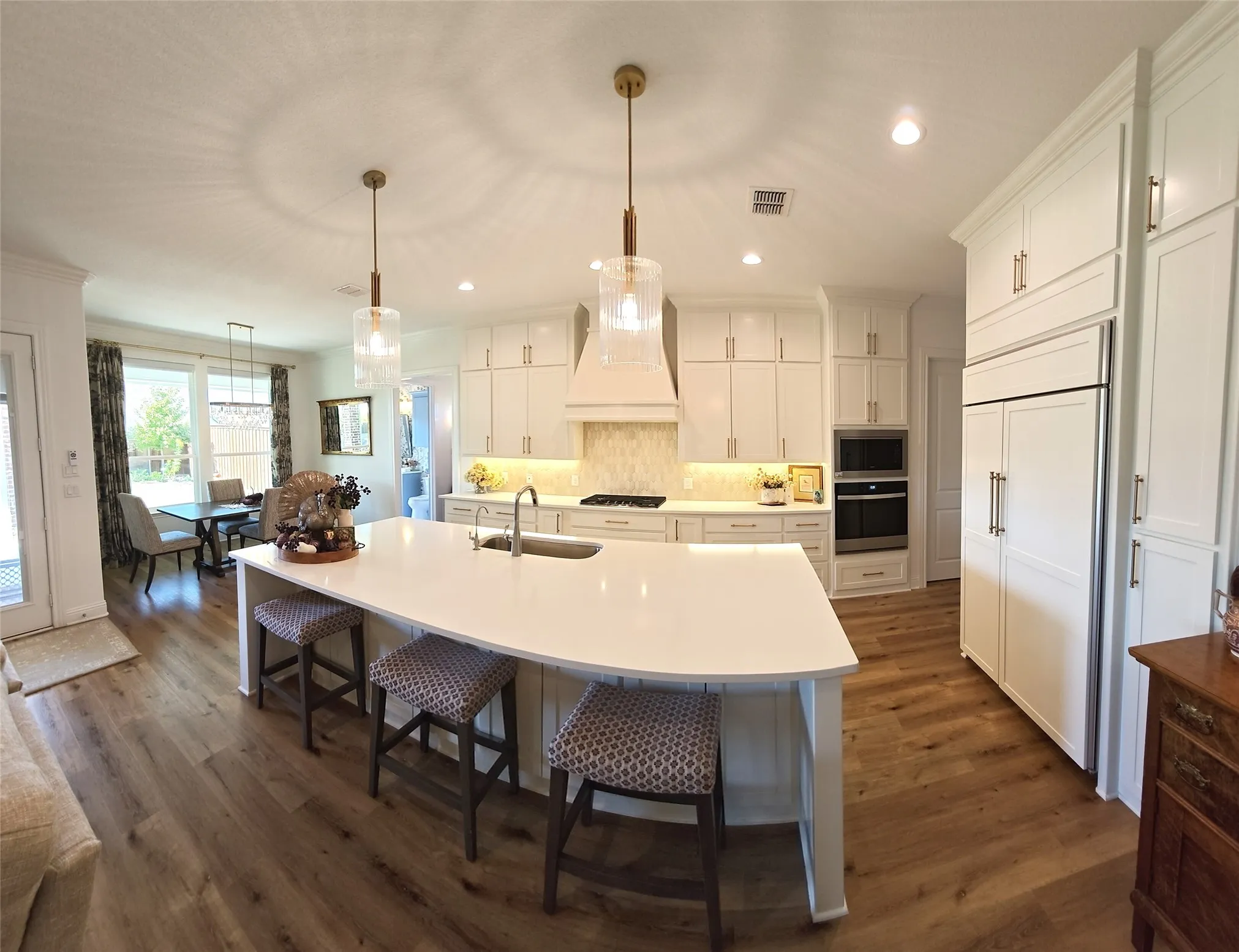 Spacious kitchen featuring an expansive island with a light-toned countertop, white cabinetry with gold-toned hardware, wood-finish flooring, and integrated stainless steel appliances