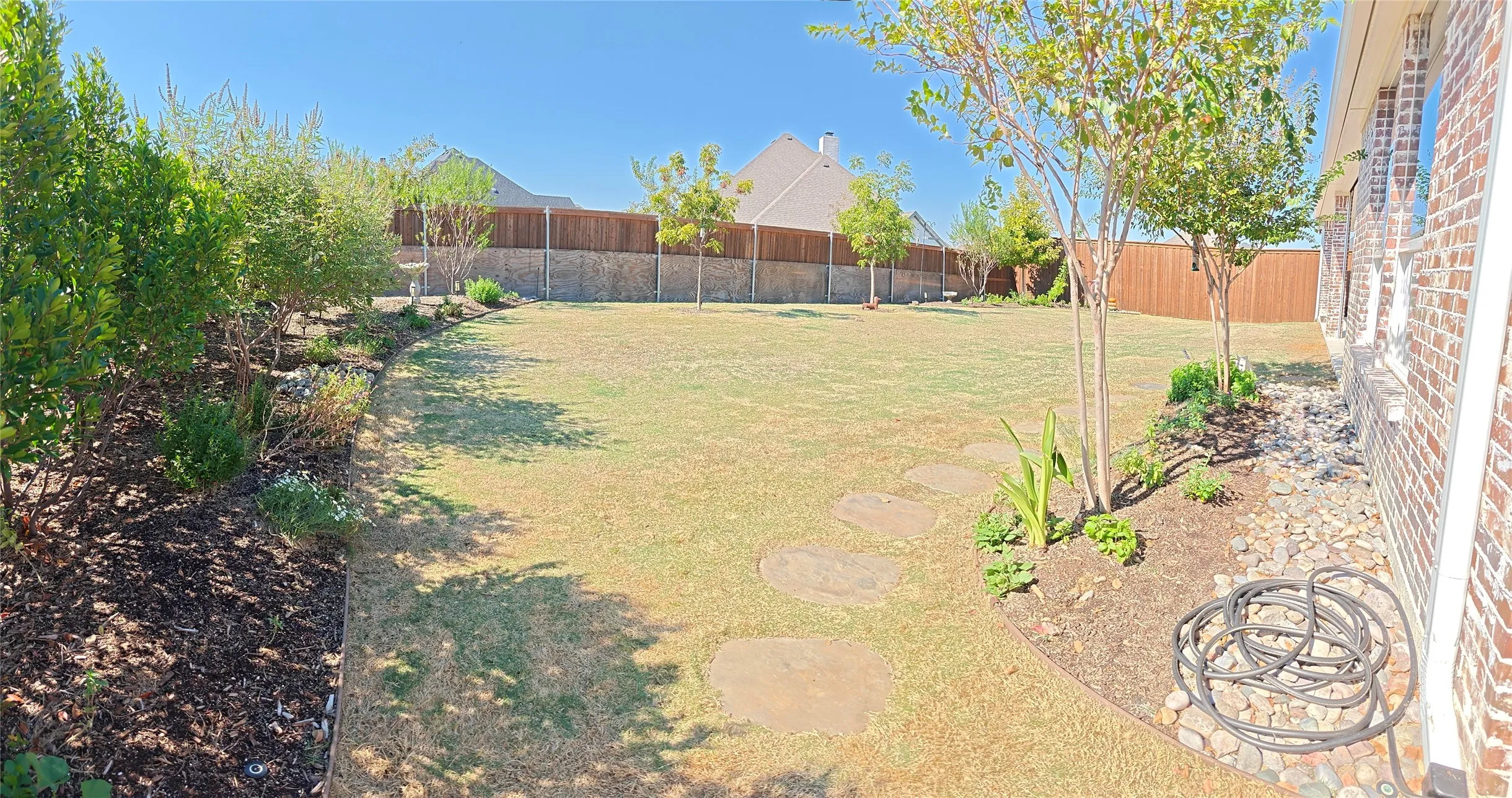 Expansive backyard featuring a manicured lawn, established landscaping beds, and a wood privacy fence