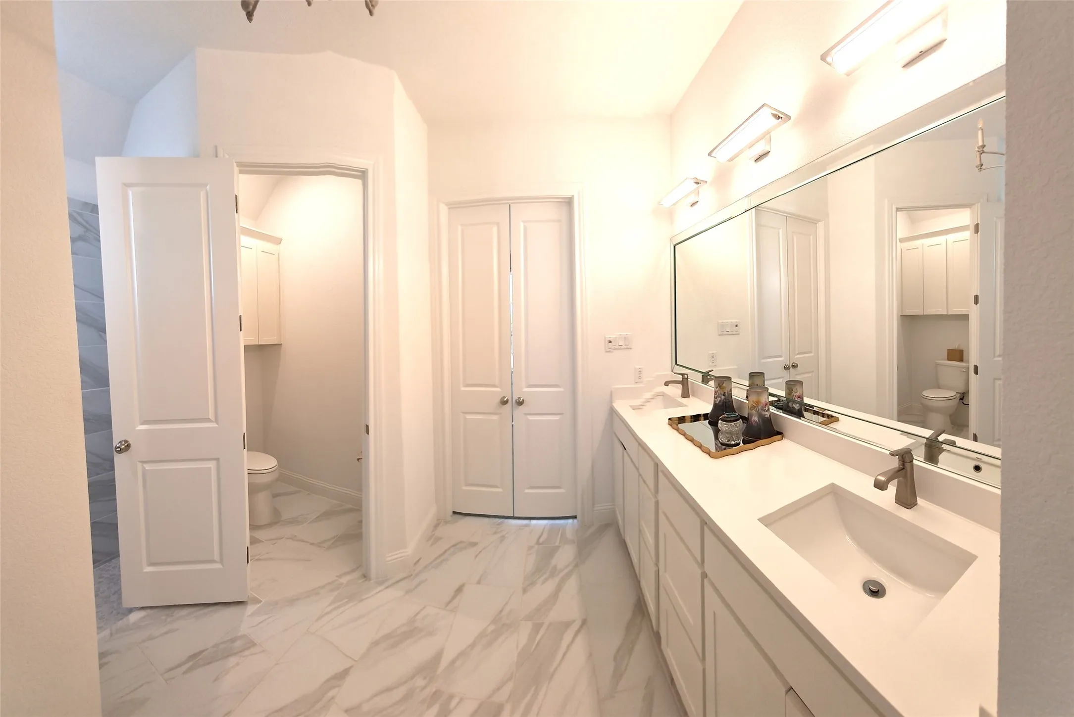 Spacious bathroom featuring a dual vanity with undermount sinks, an expansive mirror, and a water closet with built-in cabinetry