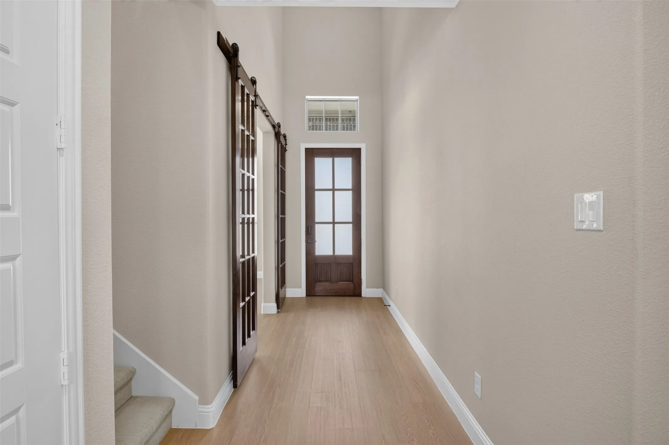 Hallway with wood-finish flooring, two dark wood barn doors, and a wood-frame door with frosted glass panels