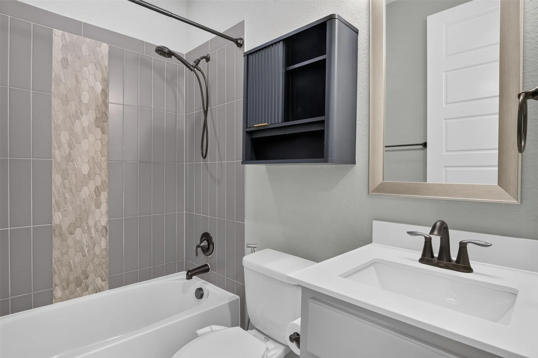 Bathroom featuring a shower-tub combination, vertical tile surround with an accent mosaic, white vanity with an integrated sink, and dark bronze fixtures