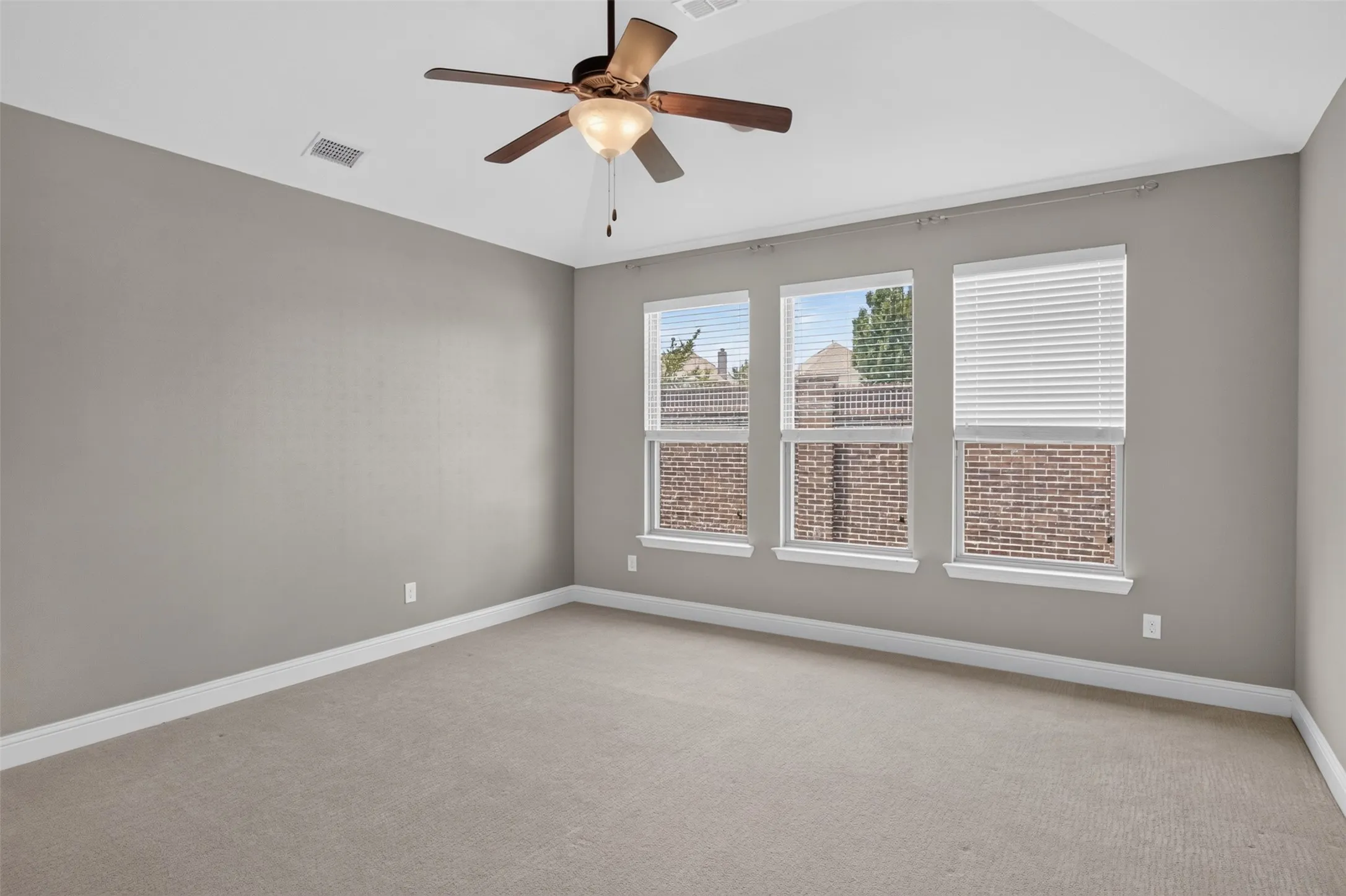Carpeted room featuring three windows with blinds, a ceiling fan, and tray ceiling