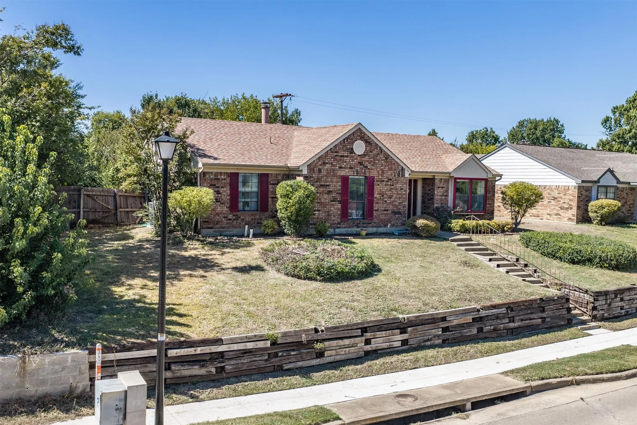Brick exterior with red shutters, stepped entry with handrails, and a terraced front yard featuring a wood retaining wall