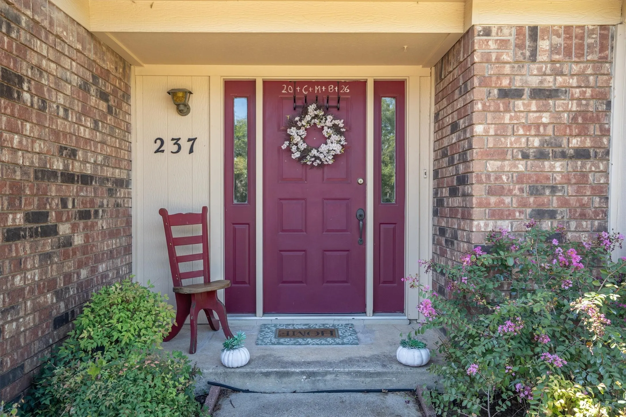 Brick exterior with a plum-colored entry door, adjacent sidelights, and mature landscaping