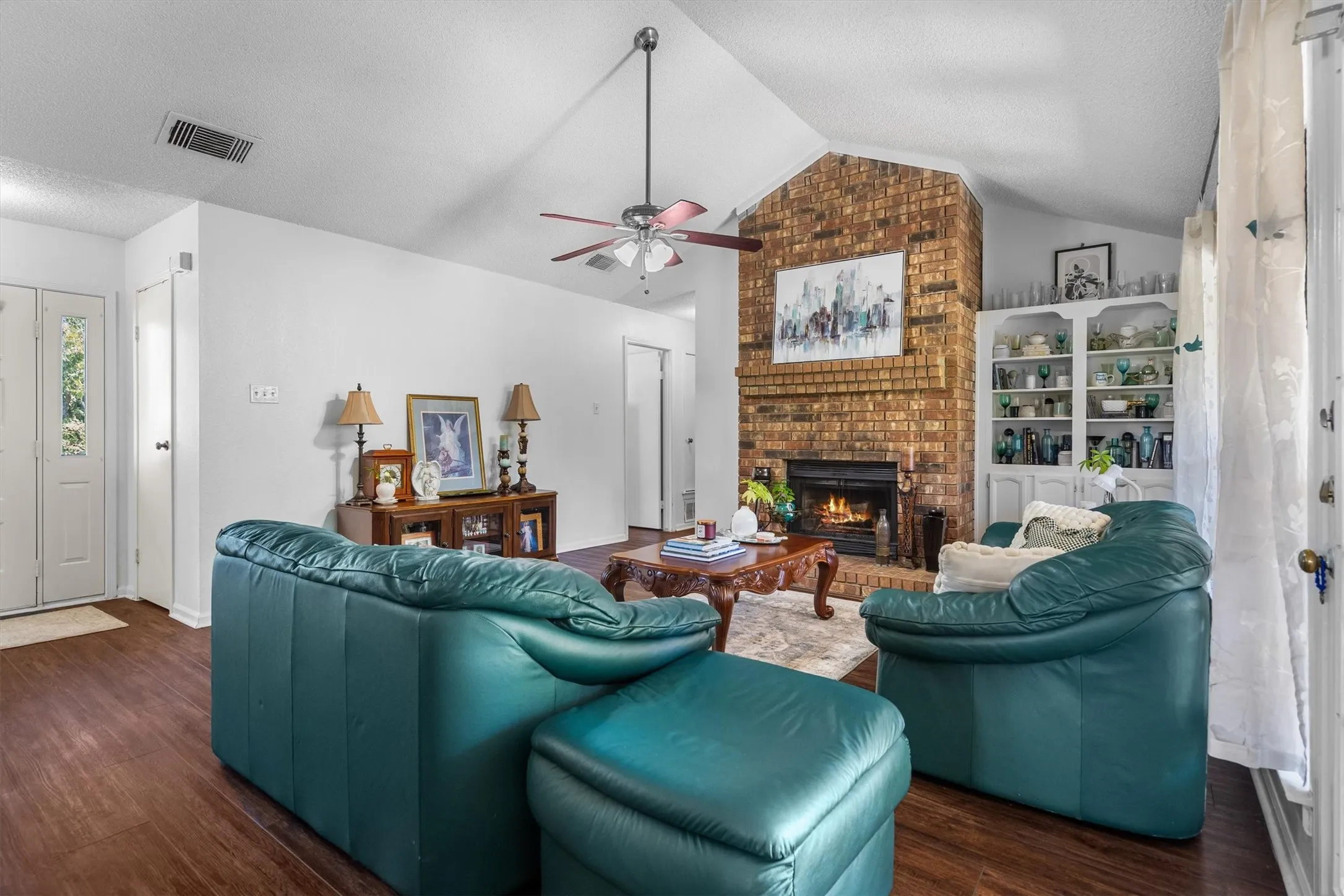 Living area featuring wood-finish flooring, vaulted ceiling, and a brick fireplace