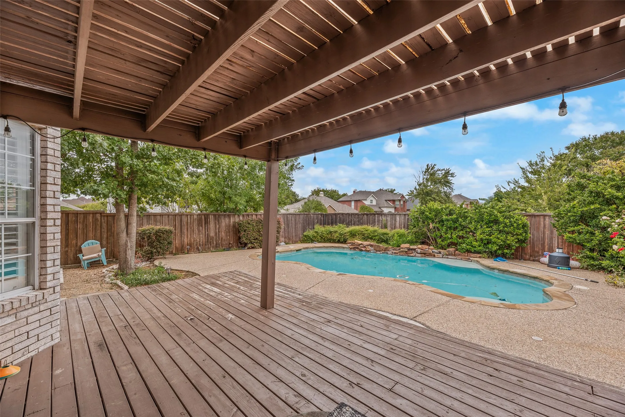 Expansive outdoor living area featuring a covered wood deck, a sparkling swimming pool, a rock waterfall, and privacy fencing