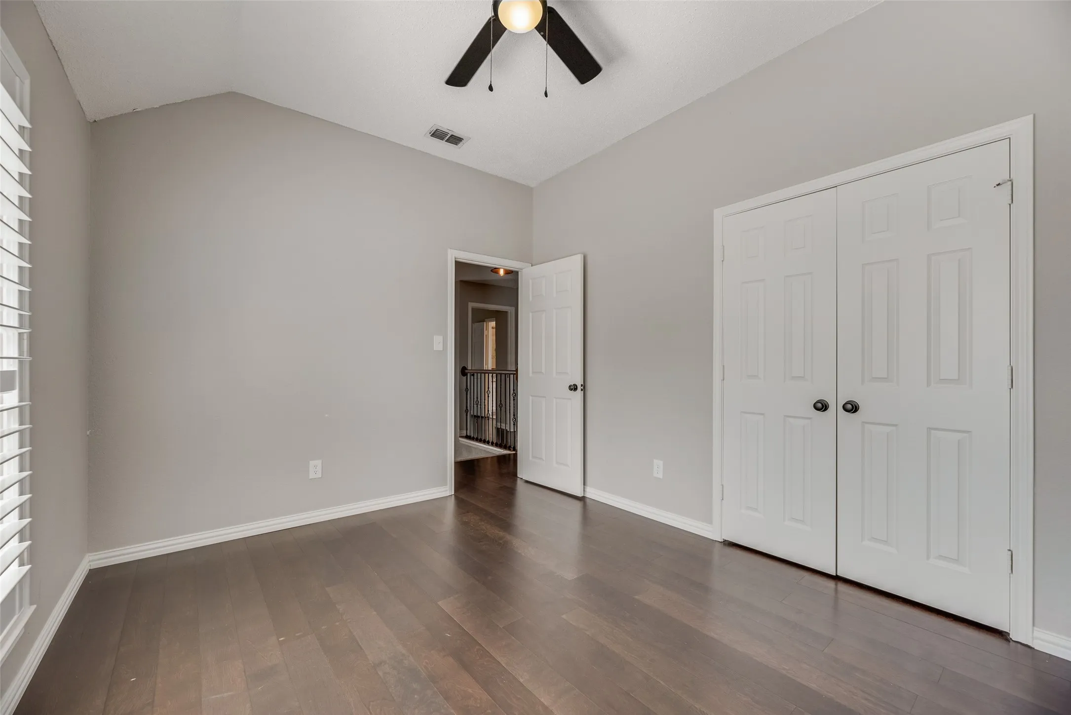 Vaulted ceiling with a ceiling fan, dark wood-finish flooring, and white bi-fold closet doors