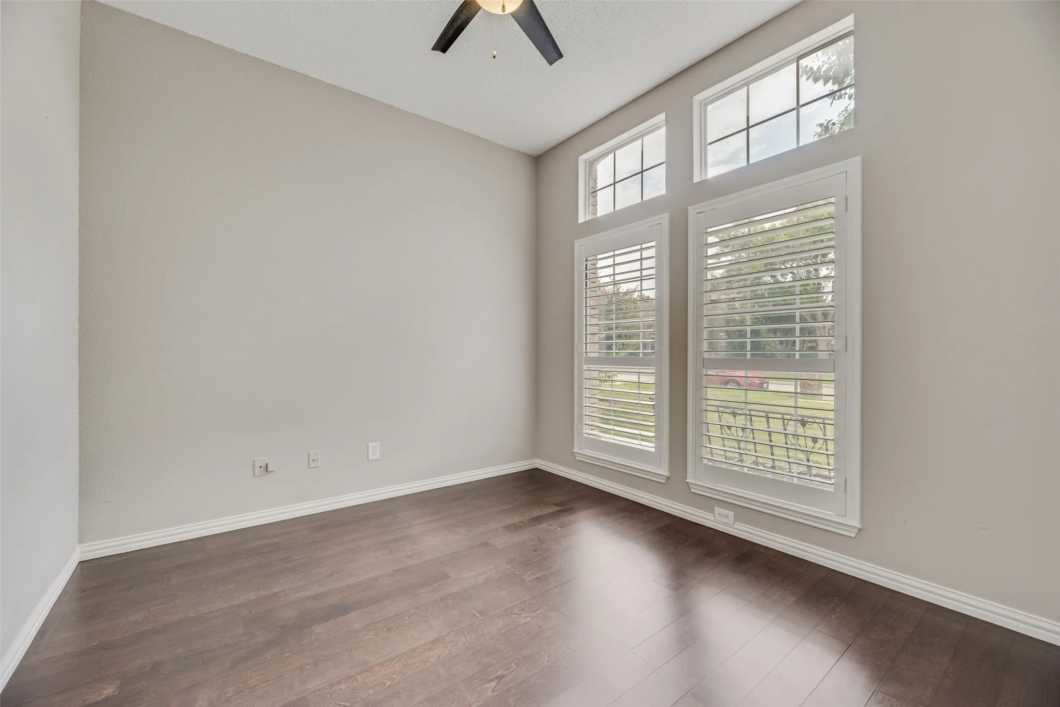 Wood-finish flooring, high ceilings, large windows with plantation shutters, and a ceiling fan