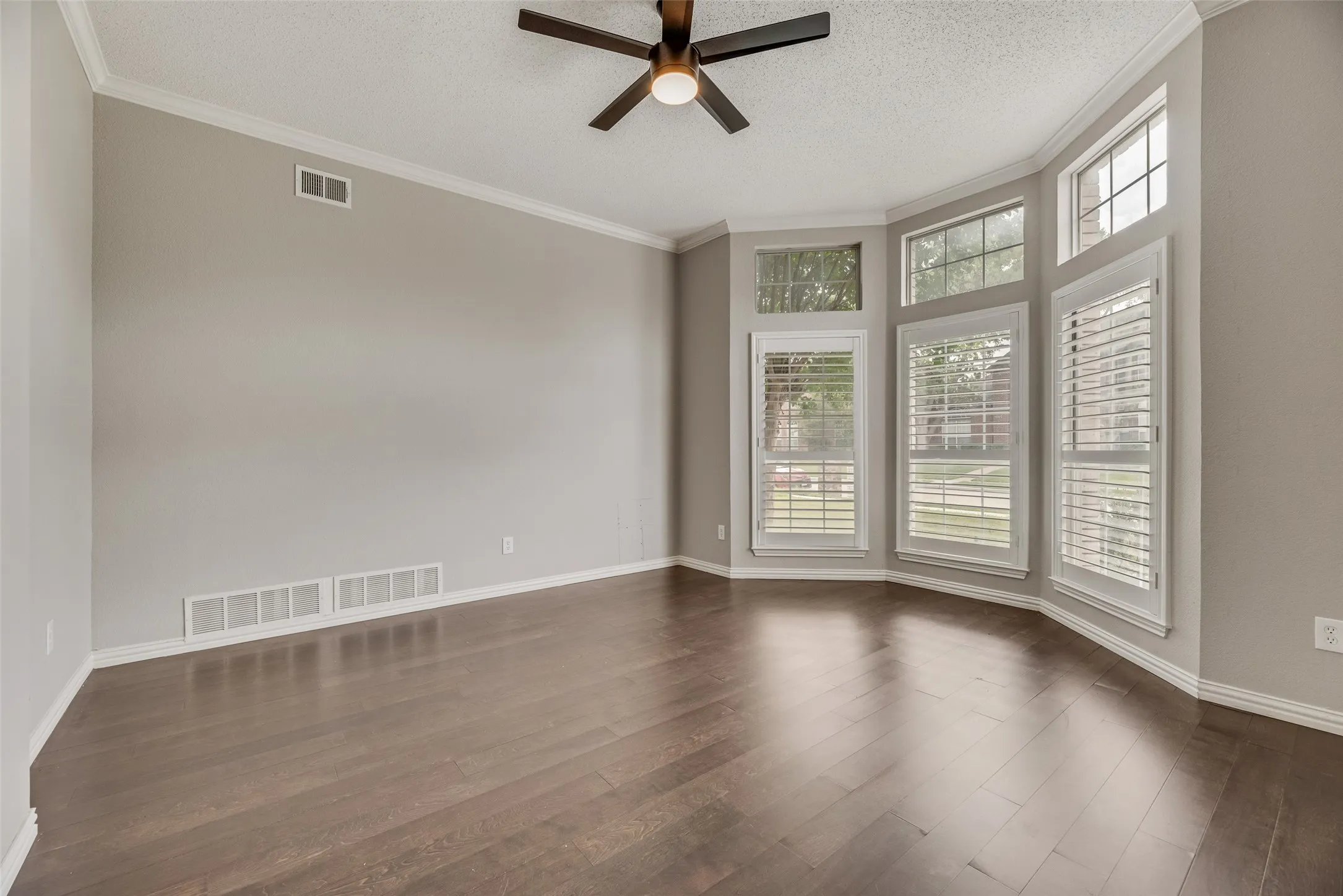Wood-finish flooring, bay window with plantation shutters, ceiling fan, and crown molding