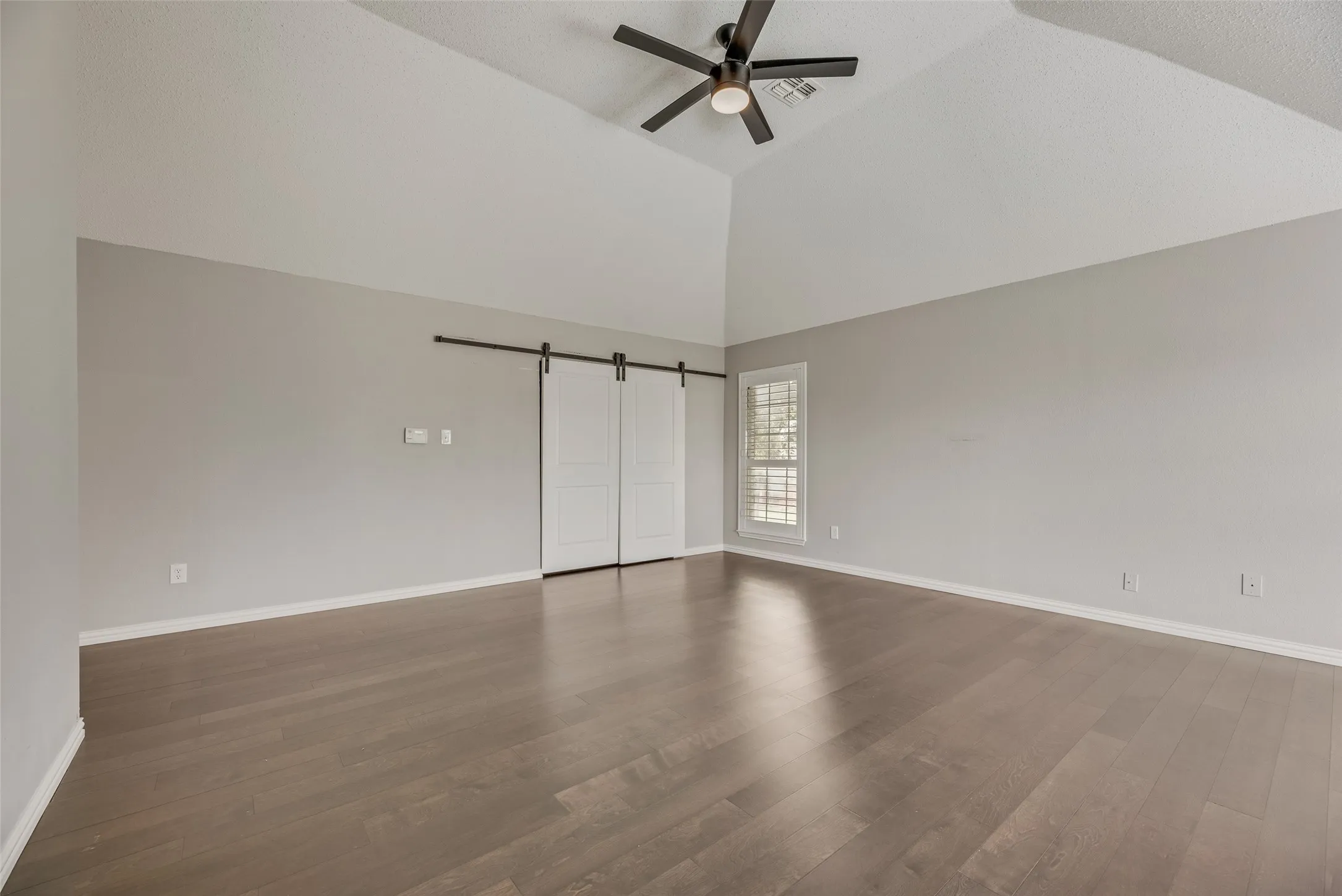 Vaulted ceiling, wood-finish flooring, ceiling fan, white plantation shutters, and barn doors