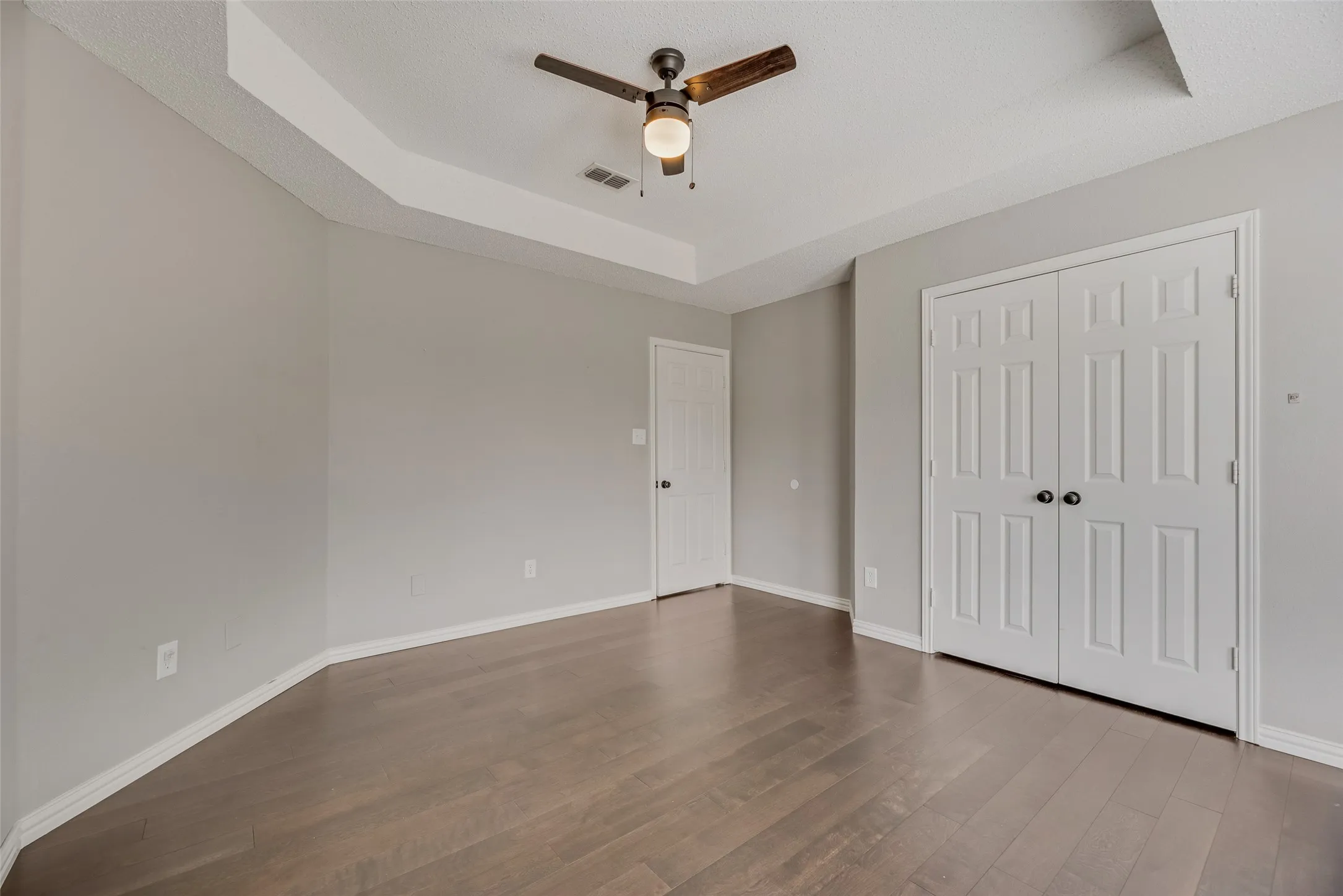 Wood-finish flooring, tray ceiling, ceiling fan with light, and paneled bifold closet doors